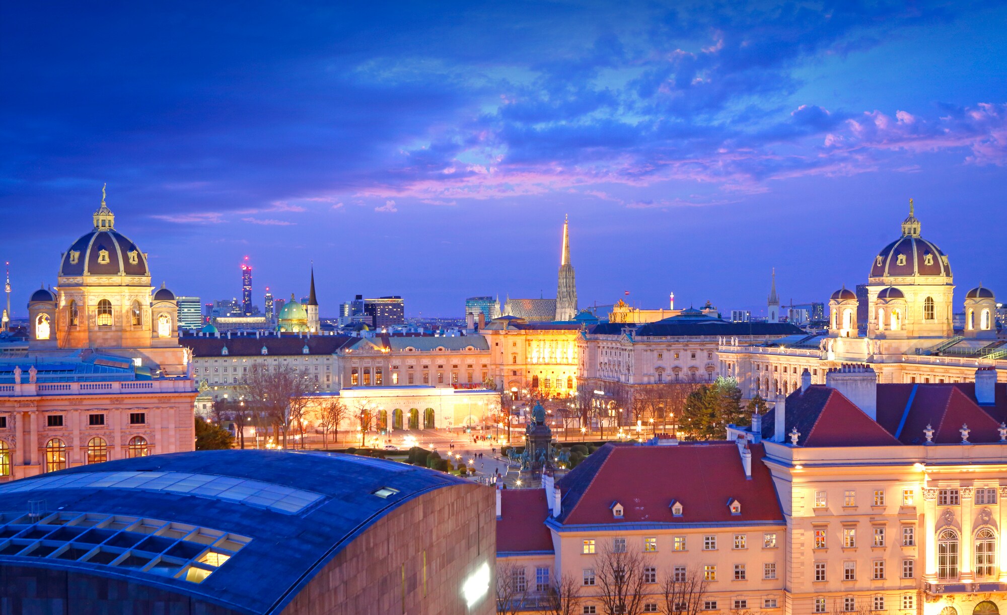 Blick von oben auf eine Stadt in der Dämmerung. Im Vordergrund sind prächtige, beleuchtete Gebäude zu sehen. Blick von oben auf eine Stadt in der Dämmerung. Im Vordergrund sind prächtige, beleuchtete Gebäude zu sehen.