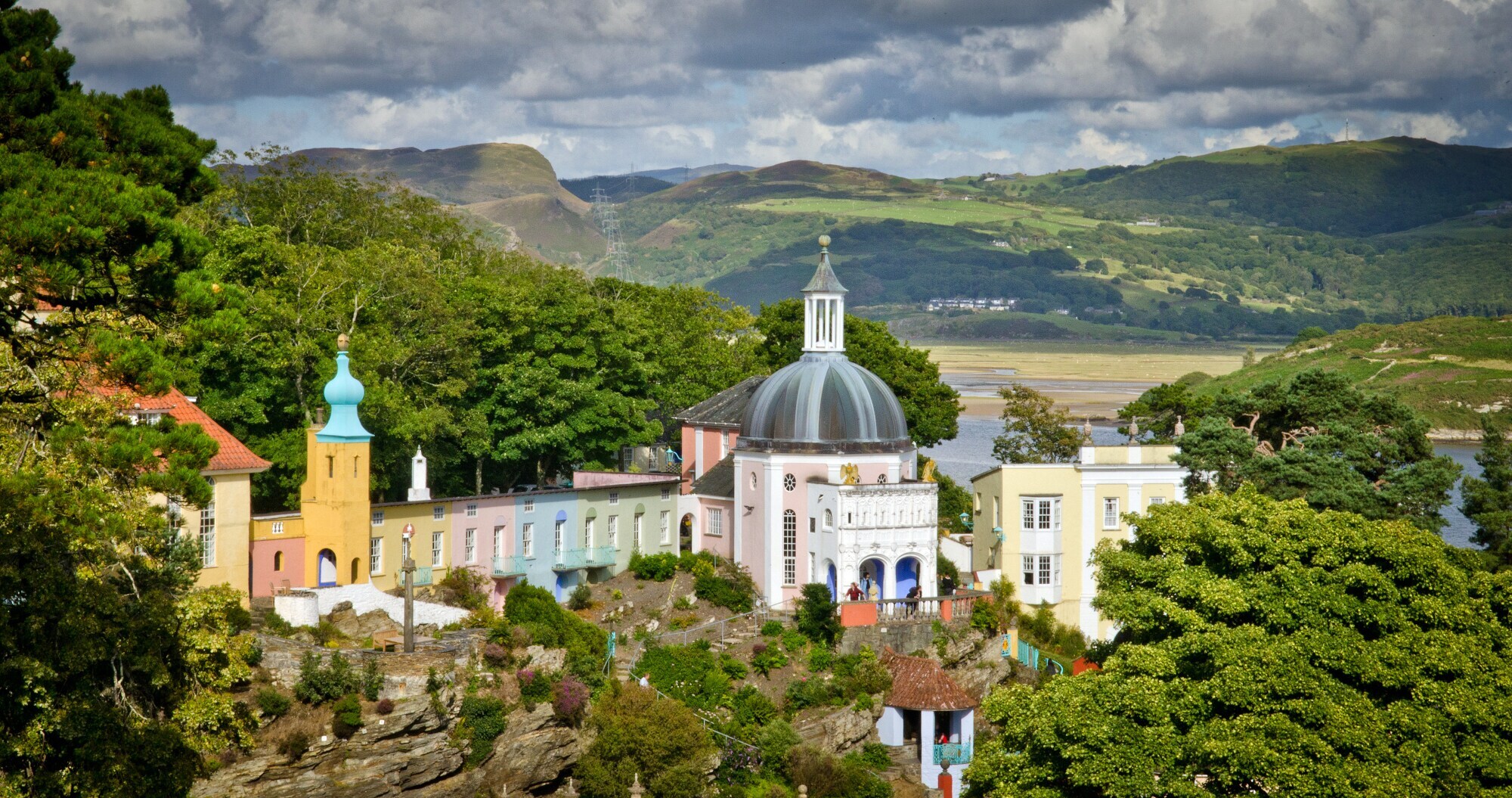 Ortschaft mit bunten Häusern und Kirchengebäude, eingebettet in grüne Hügellandschaft.