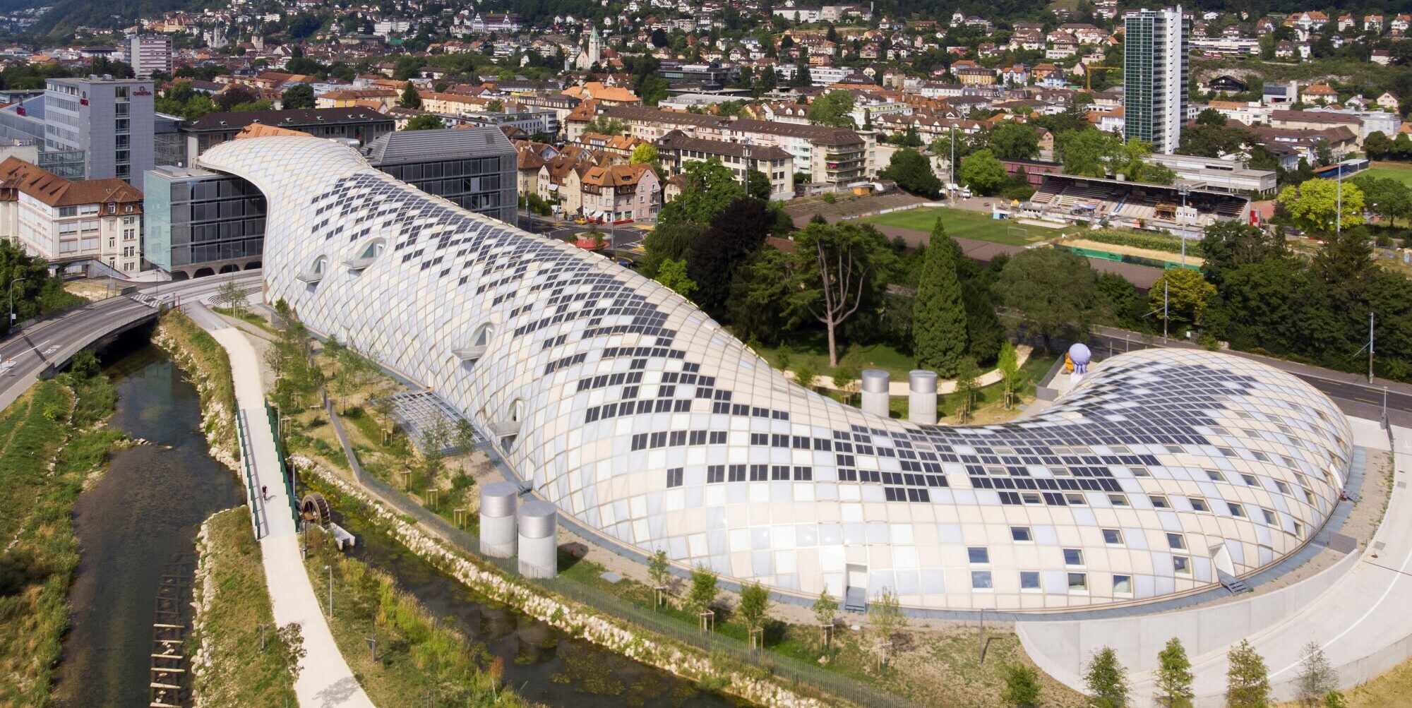 Panorama einer Kleinstadt mit futuristischem Gebäudekomplex in Schlangenform.