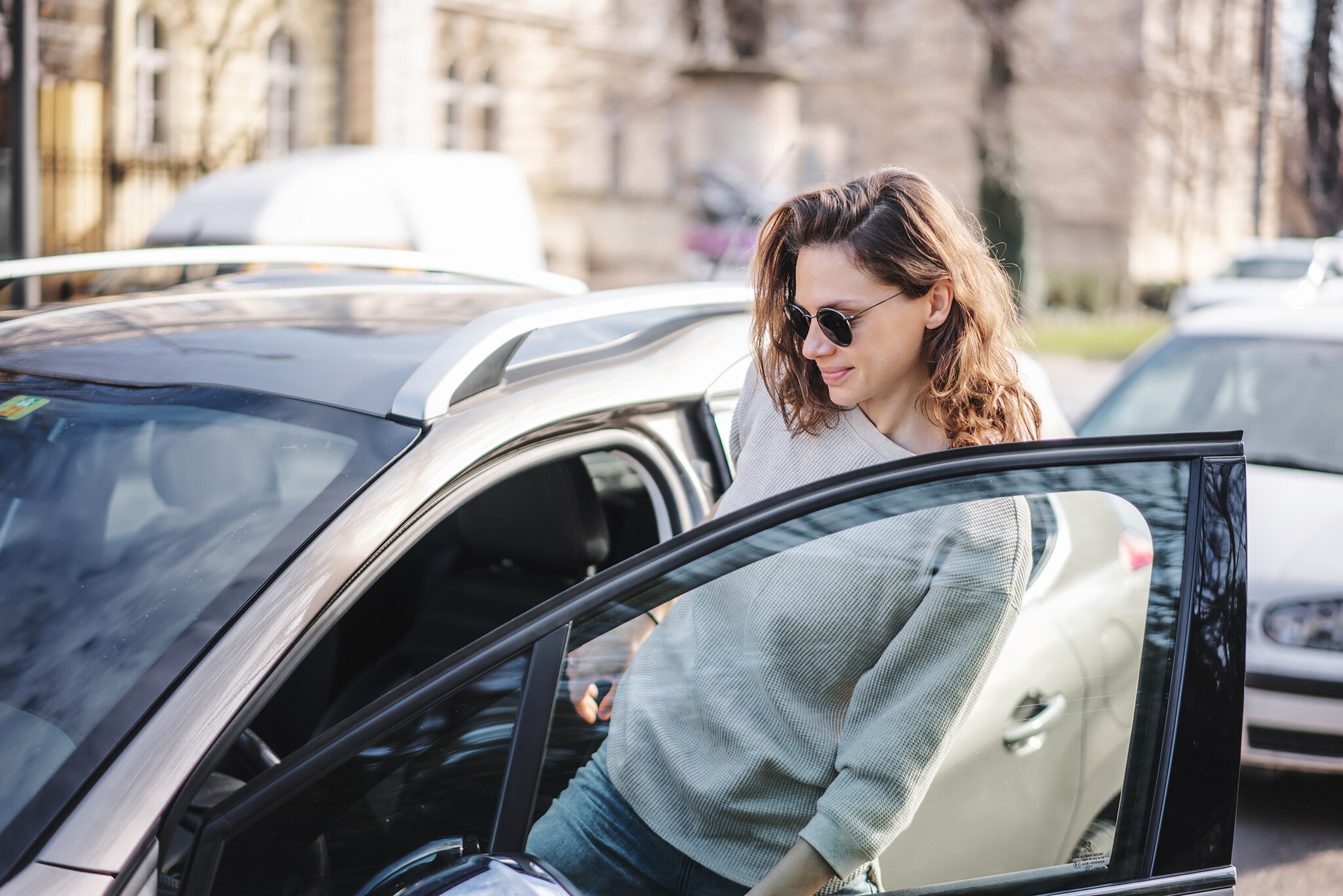 Auto-Abo als smarte Alternative zum Firmenwagen: Mobility redefined Eine Frau mit Sonnenbrille steigt in parkenden PKW ein.
