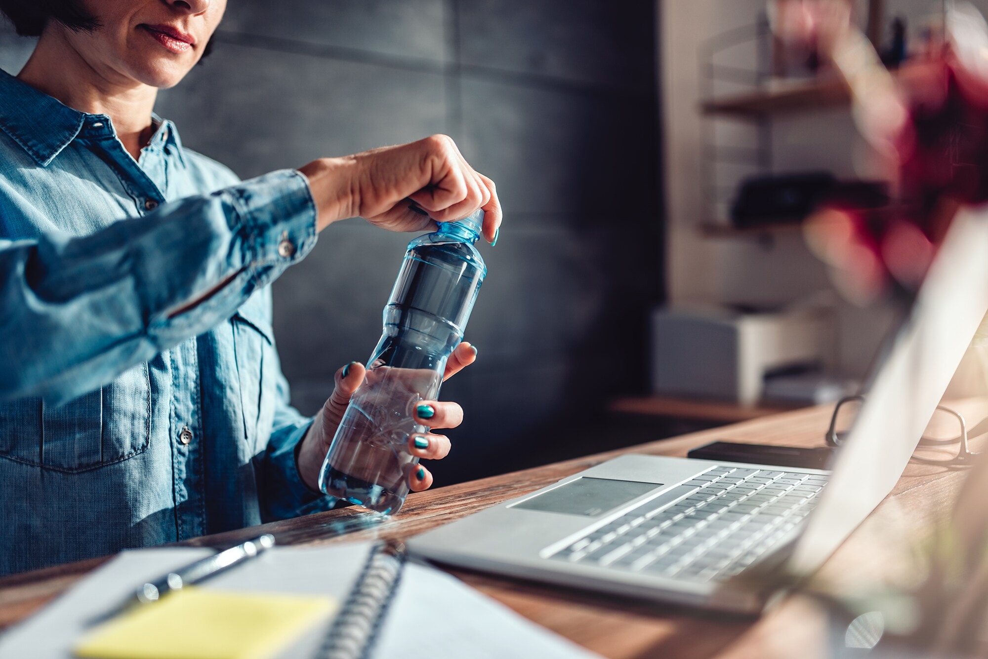 Self-Care im Home-Office: 5 Must-dos für dein Wohlbefinden Frau im Home-Office öffnet eine Wasserflasche