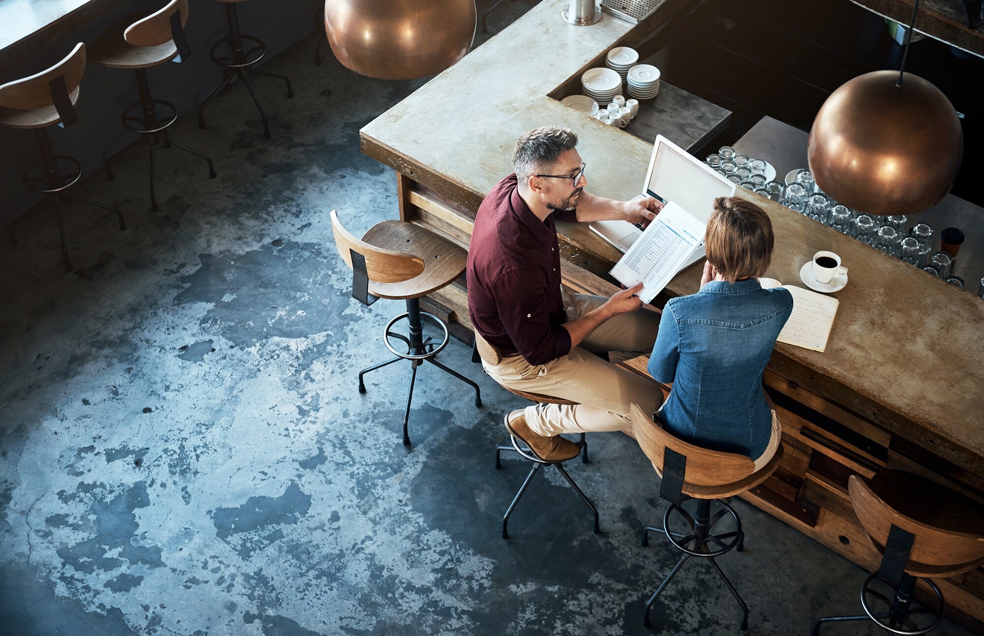Arbeiten im Café: Regeln für Produktivität mit Laptop & Latte Macchiato Zwei Geschäftsleute arbeiten am Tresen eines Cafés.