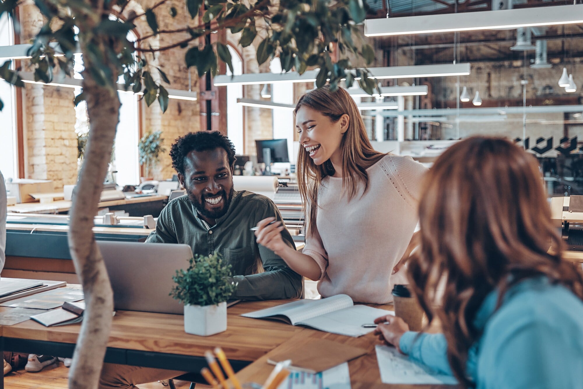 Büro einrichten: 7 Tipps für die perfekte Arbeitsatmosphäre Drei junge Geschäftsleute unterhalten sich in einem hellen, modern eingerichteten Großraumbüro.