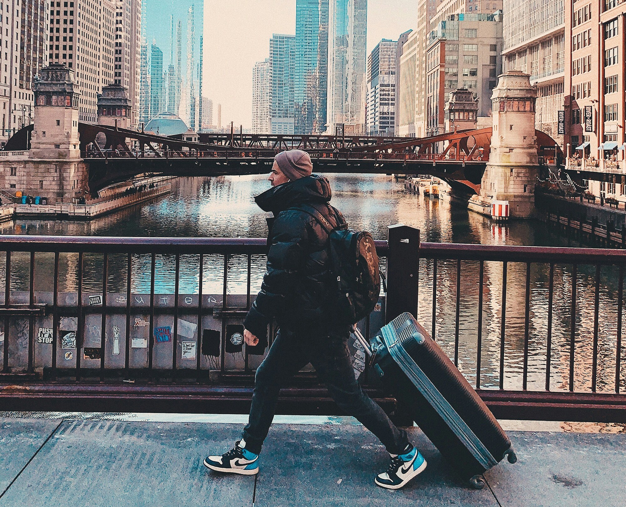 Business-Travel-Typen – welcher bist du? Ein junger Reisender mit Koffer und Rucksack überquert eine Brücke in Chicago.