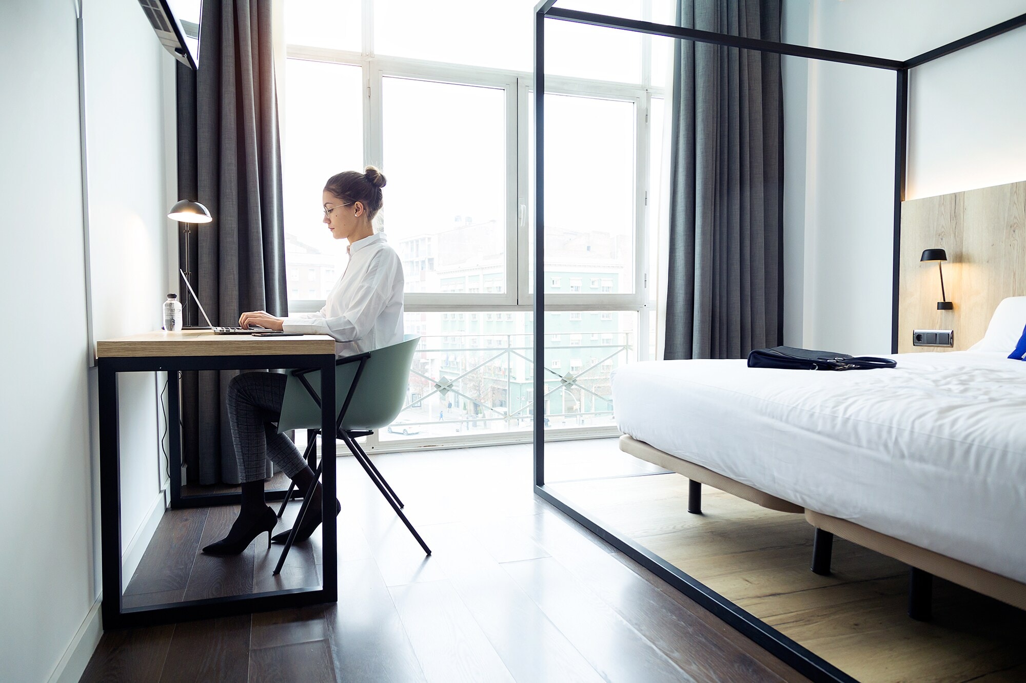 Checkliste Business Travel: Das brauchst du auf deiner Geschäftsreise wirklich Eine junge Geschäftsfrau arbeitet am Laptop in ihrem Hotelzimmer.