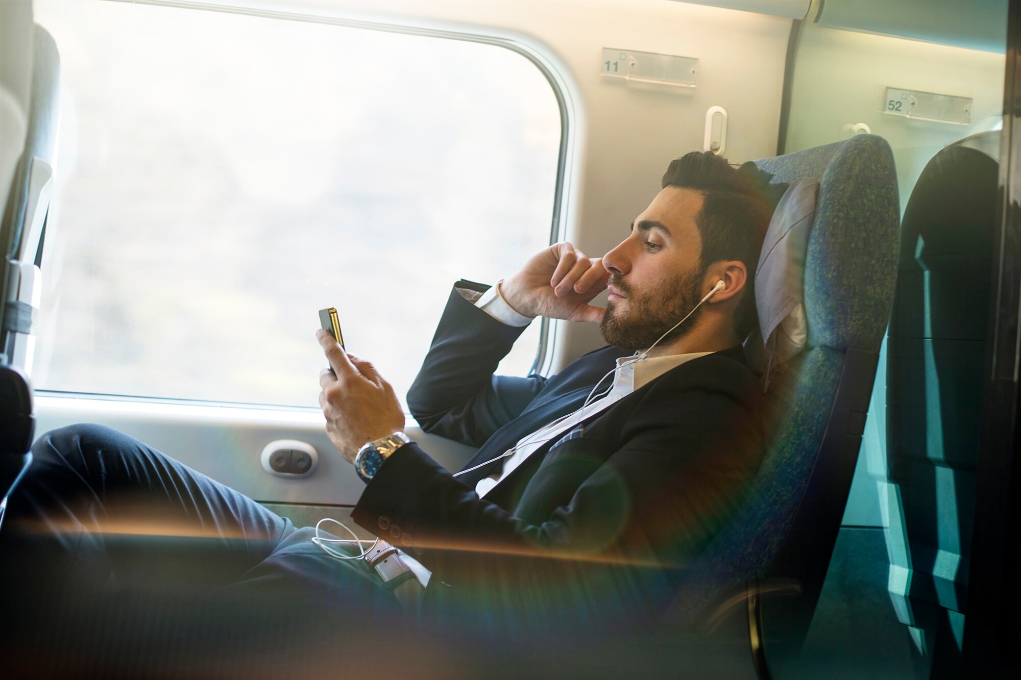 Reise-Burnout vermeiden: Diese 13 Tipps sorgen für Entspannung Ein Geschäftsmann sitzt entspannt im Zug und hört Musik