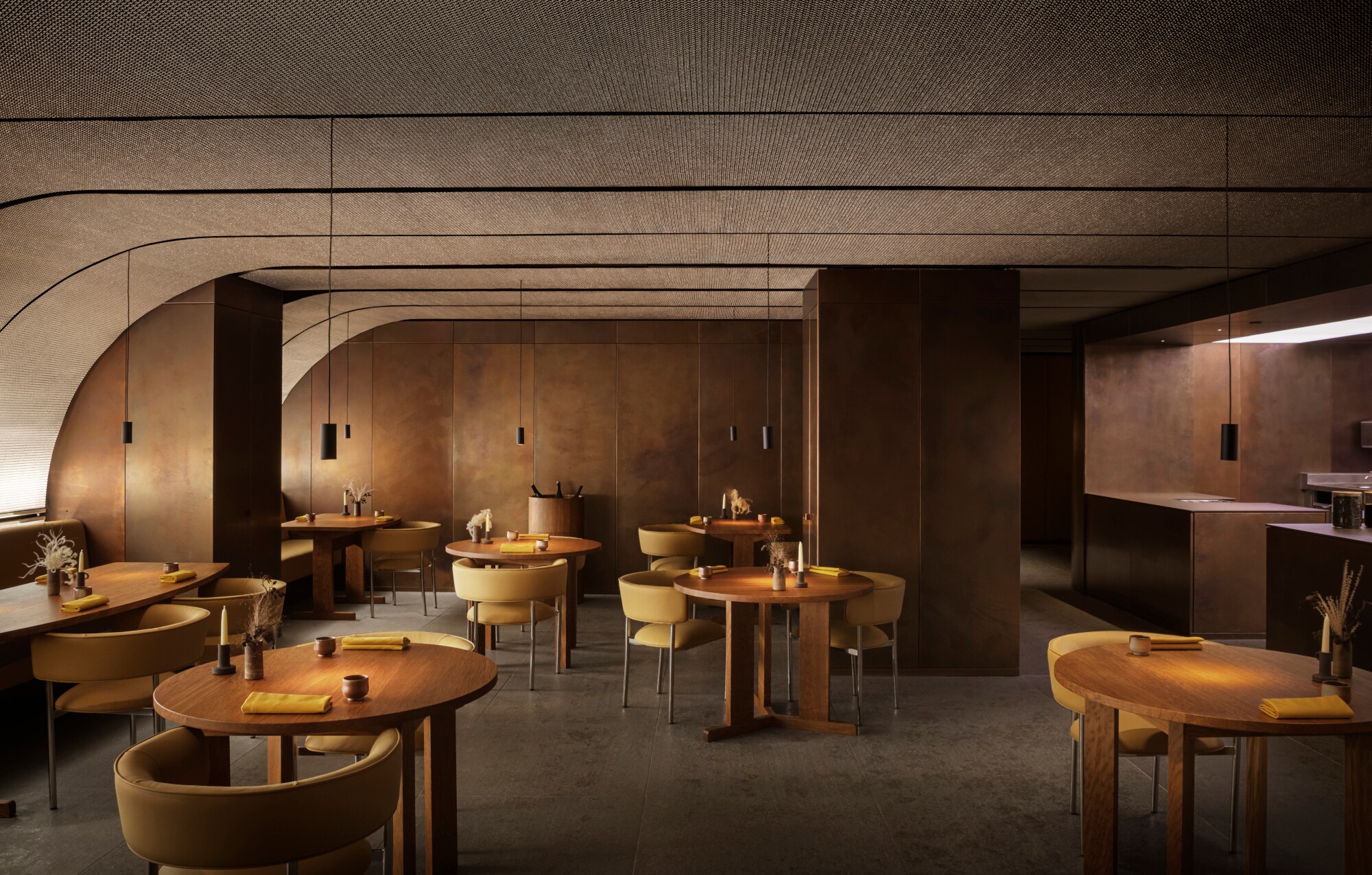 Ein minimalistisch eingerichteter Raum mit runden Holztischen und abgerundeter Decke.