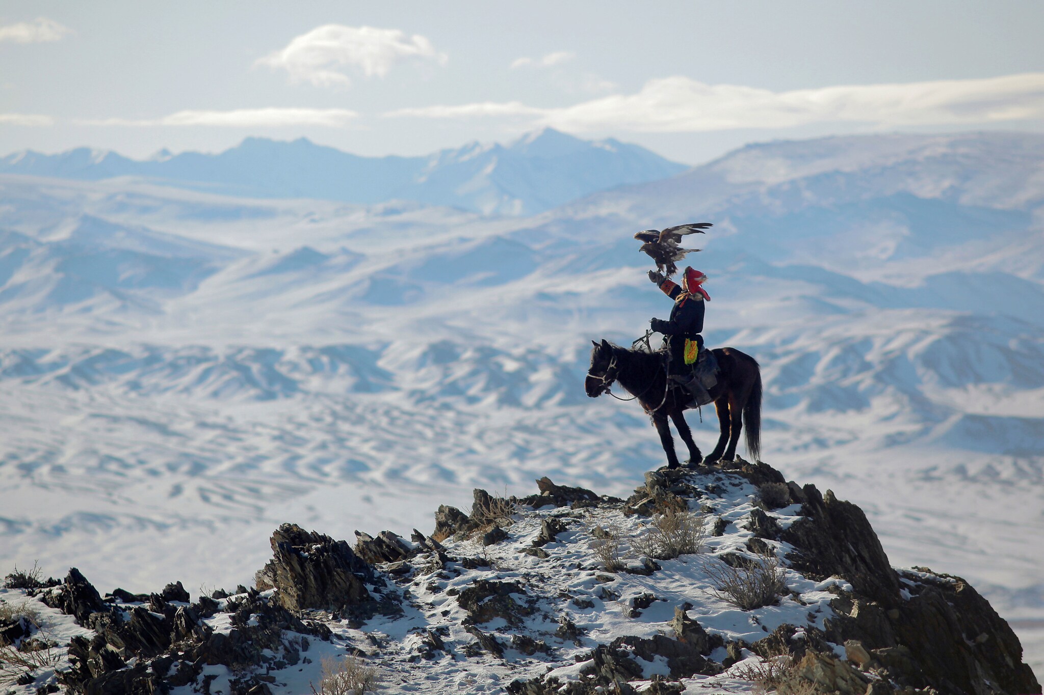 Ein Mann sitzt auf einem Pferd im Gebirge, auf seinem ausgestreckten Arm steht ein Adler.