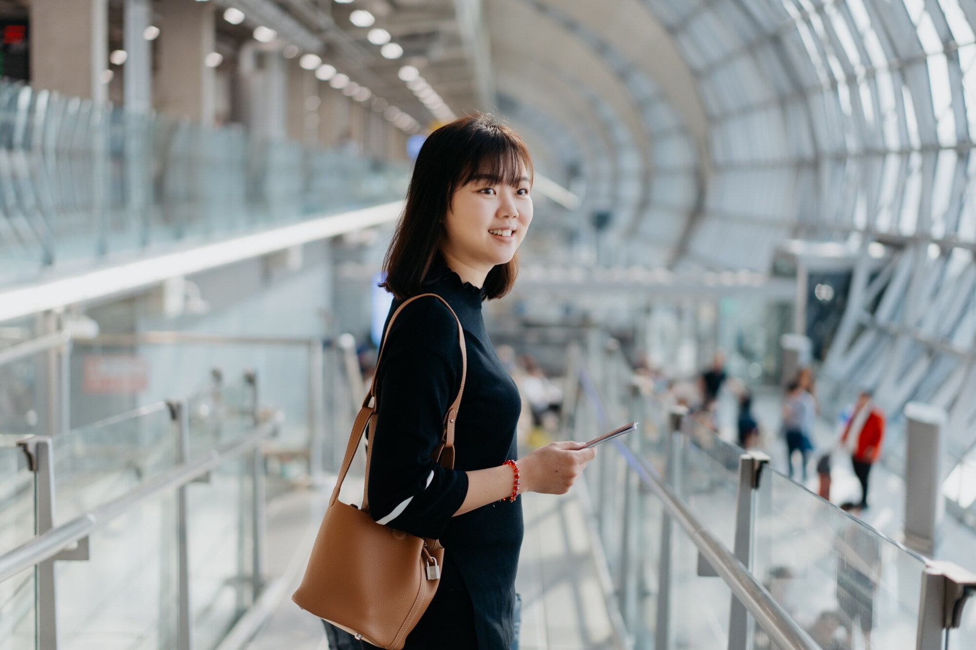 Eine lächelnde asiatische Frau steht in einem Flughafenterminal mit abgerundeter Fassade. Eine lächelnde asiatische Frau steht in einem Flughafenterminal mit abgerundeter Fassade.