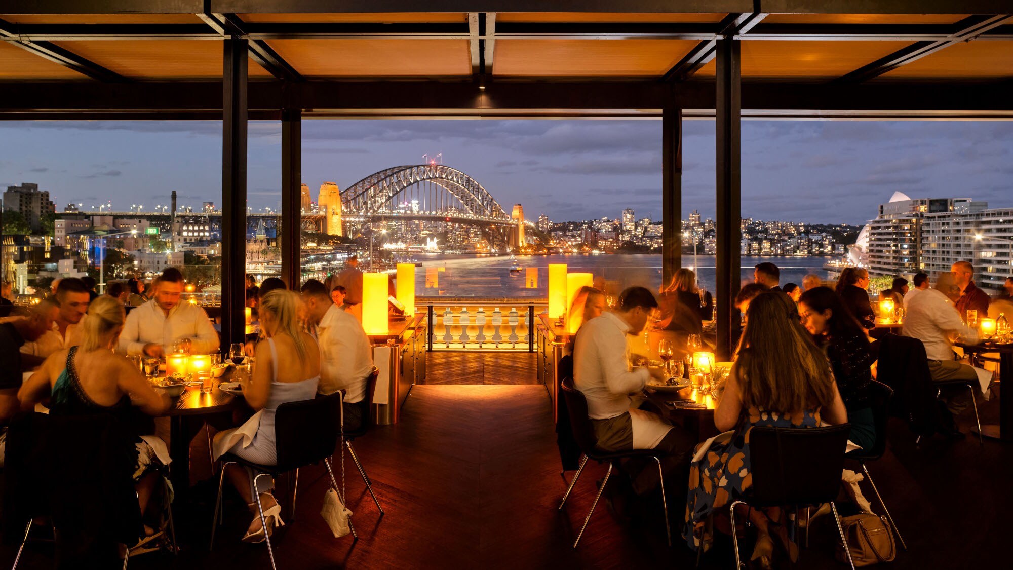 Außengastronomie am Hafen von Sydney vor beleuchteter Harbour Bridge bei Nacht.