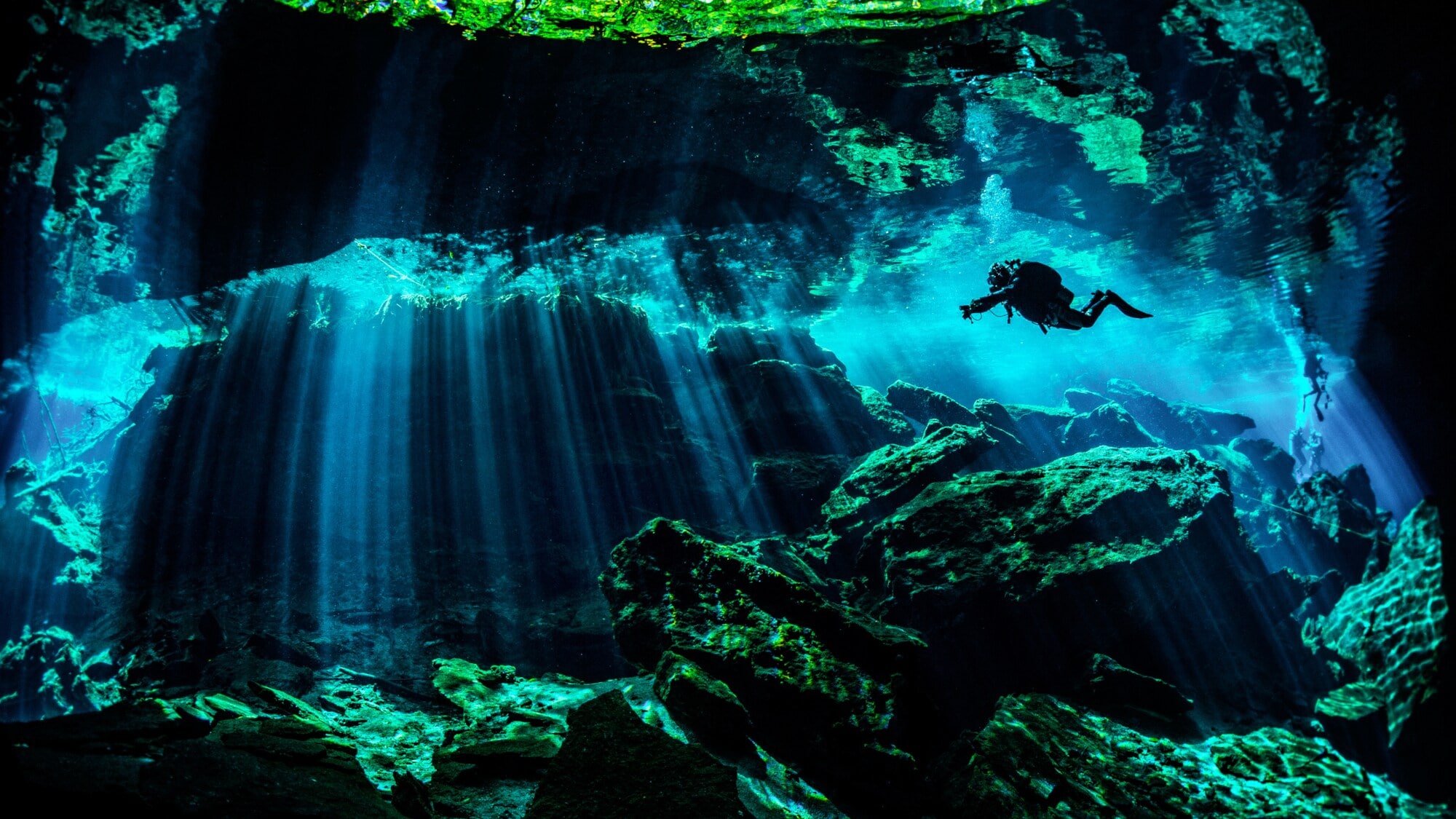 Eine Person in Taucherausrüstung taucht in einer von Wasser gefüllten Höhle. Lichtsäulen ergeben sich durch den starken Lichteinfall von oben im Wasser. Eine Person in Taucherausrüstung taucht in einer von Wasser gefüllten Höhle. Lichtsäulen ergeben sich durch den starken Lichteinfall von oben im Wasser.