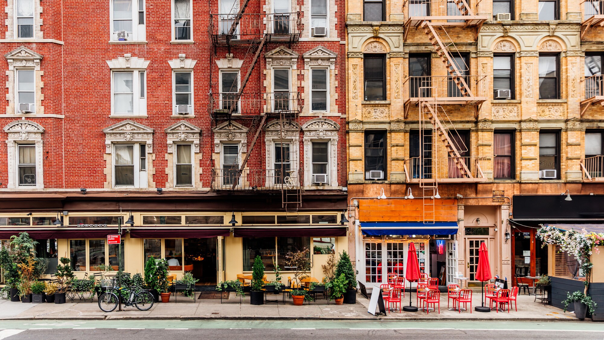 Geschlossene New Yorker Häuserfront mit Feuerleitern und Restaurants mit Außengastronomie. Geschlossene New Yorker Häuserfront mit Feuerleitern und Restaurants mit Außengastronomie.