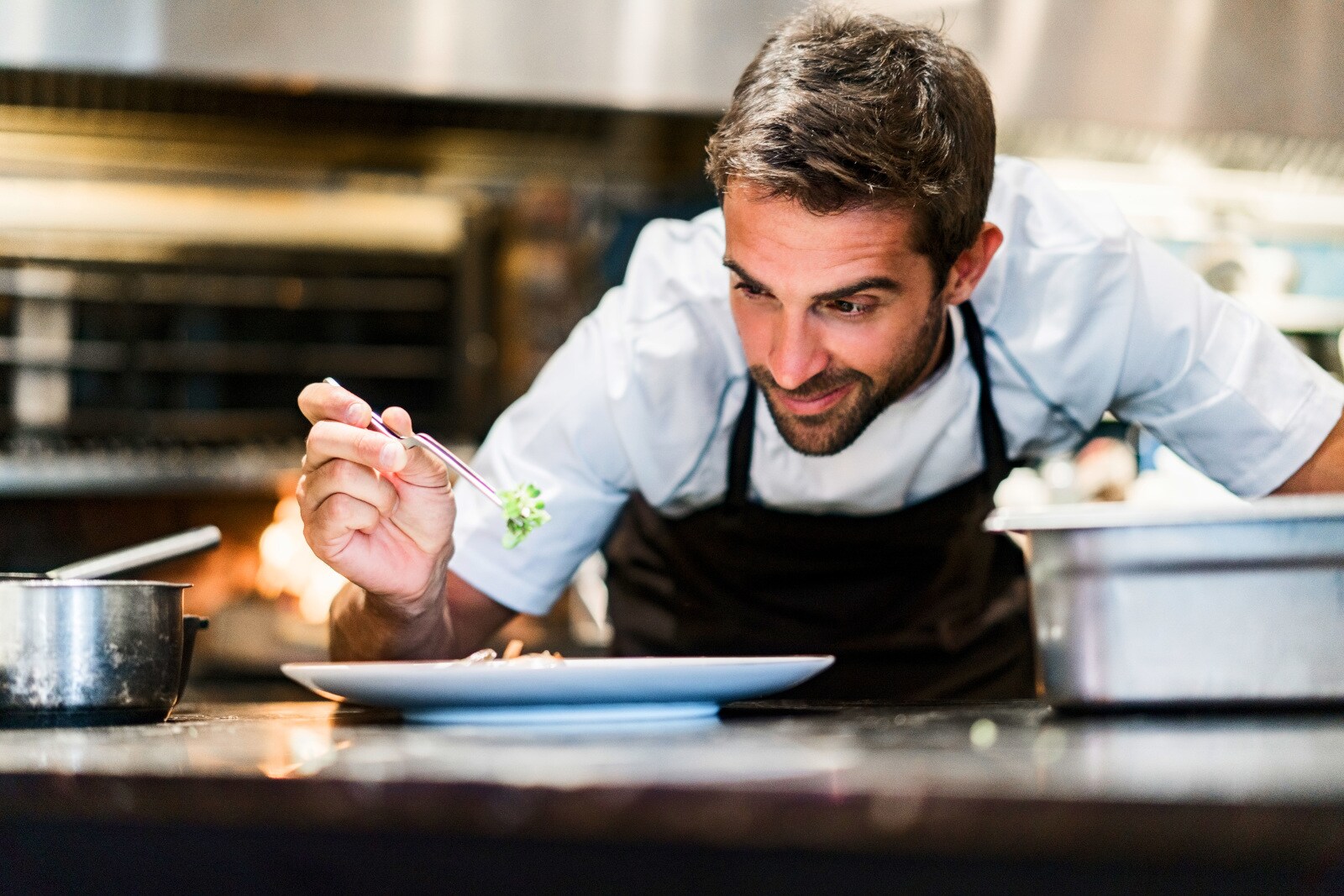 Ein Mann garniert ein Gericht auf einem weißen Teller in einer Restaurantküche. Ein Mann garniert ein Gericht auf einem weißen Teller in einer Restaurantküche.