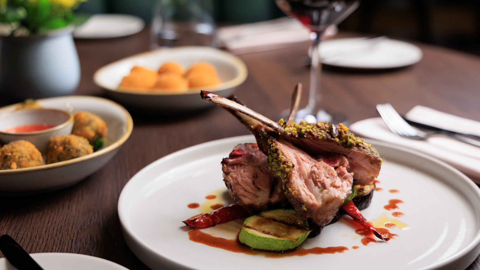 Gegrilltes Lammrippenkotelett, angerichtet auf einem weißen Teller, daneben Beilagen auf einem Tisch in einem Restaurant.