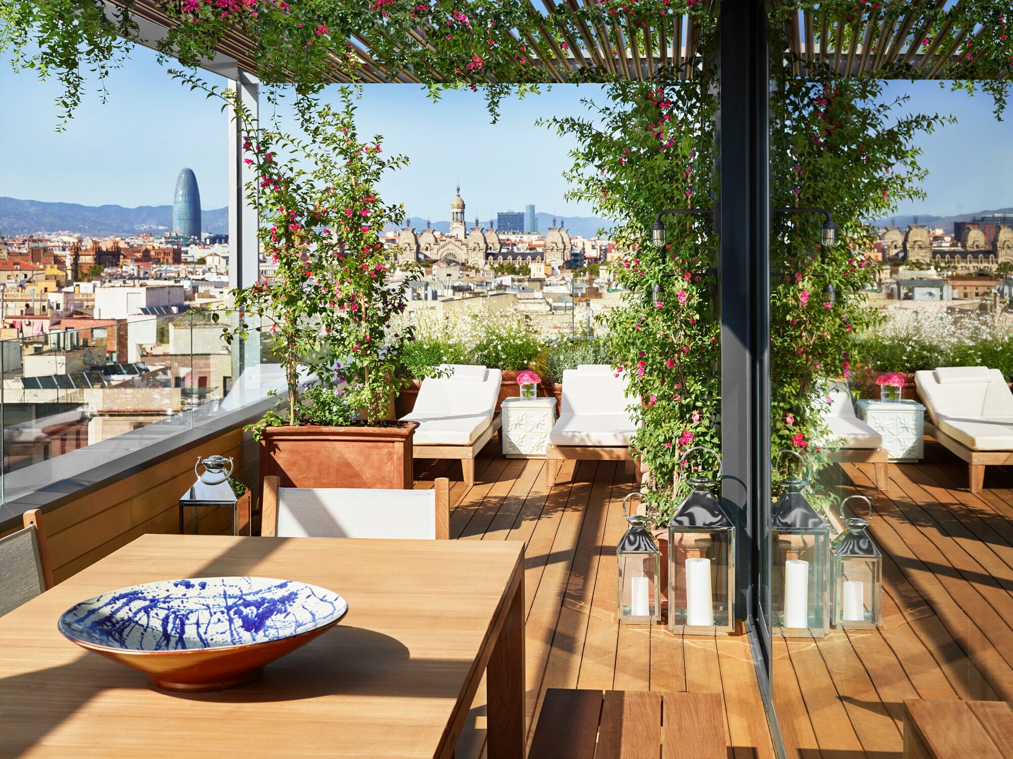 Hotelterrasse mit Liegen vor der Skyline Barcelonas bei Sonnenschein.