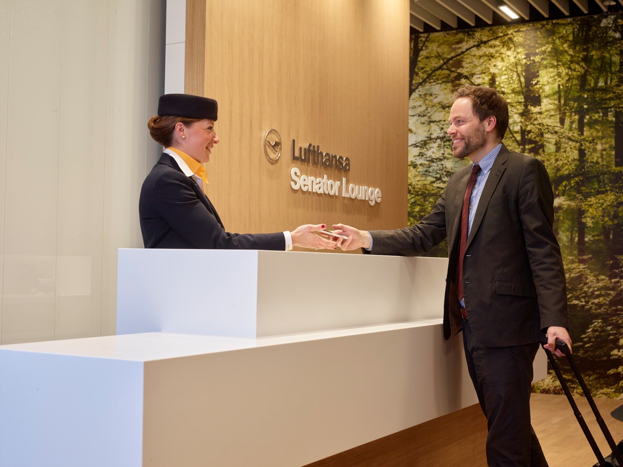 Eine Bodenstewardess begrüßt einen Gast beim Check-in am Empfang einer Lufthansa Senator Flughafenlounge. Eine Bodenstewardess begrüßt einen Gast beim Check-in am Empfang einer Lufthansa Senator Flughafenlounge.