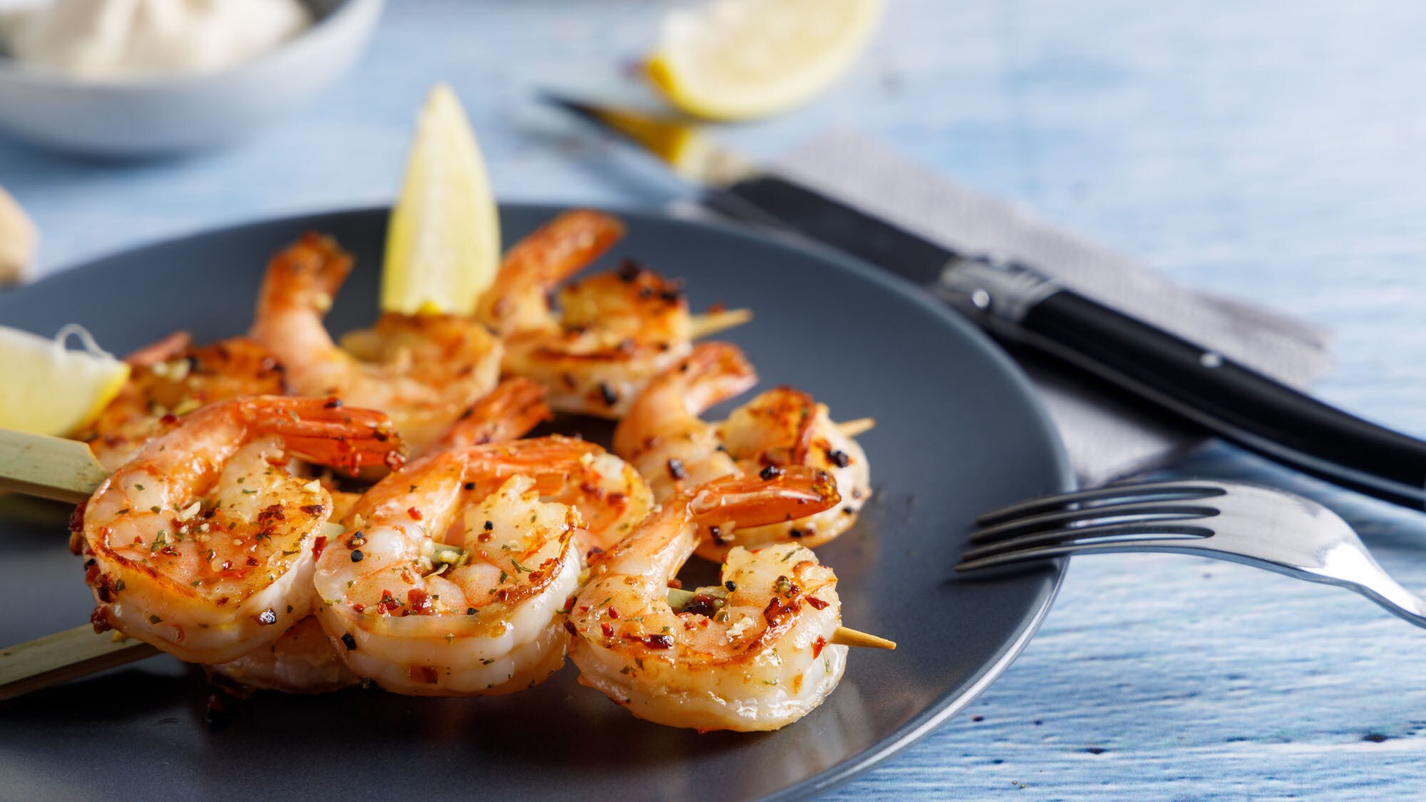 Gebratene Garnelen auf einem Spieß auf einem Teller, garniert mit Zitronenstücken.