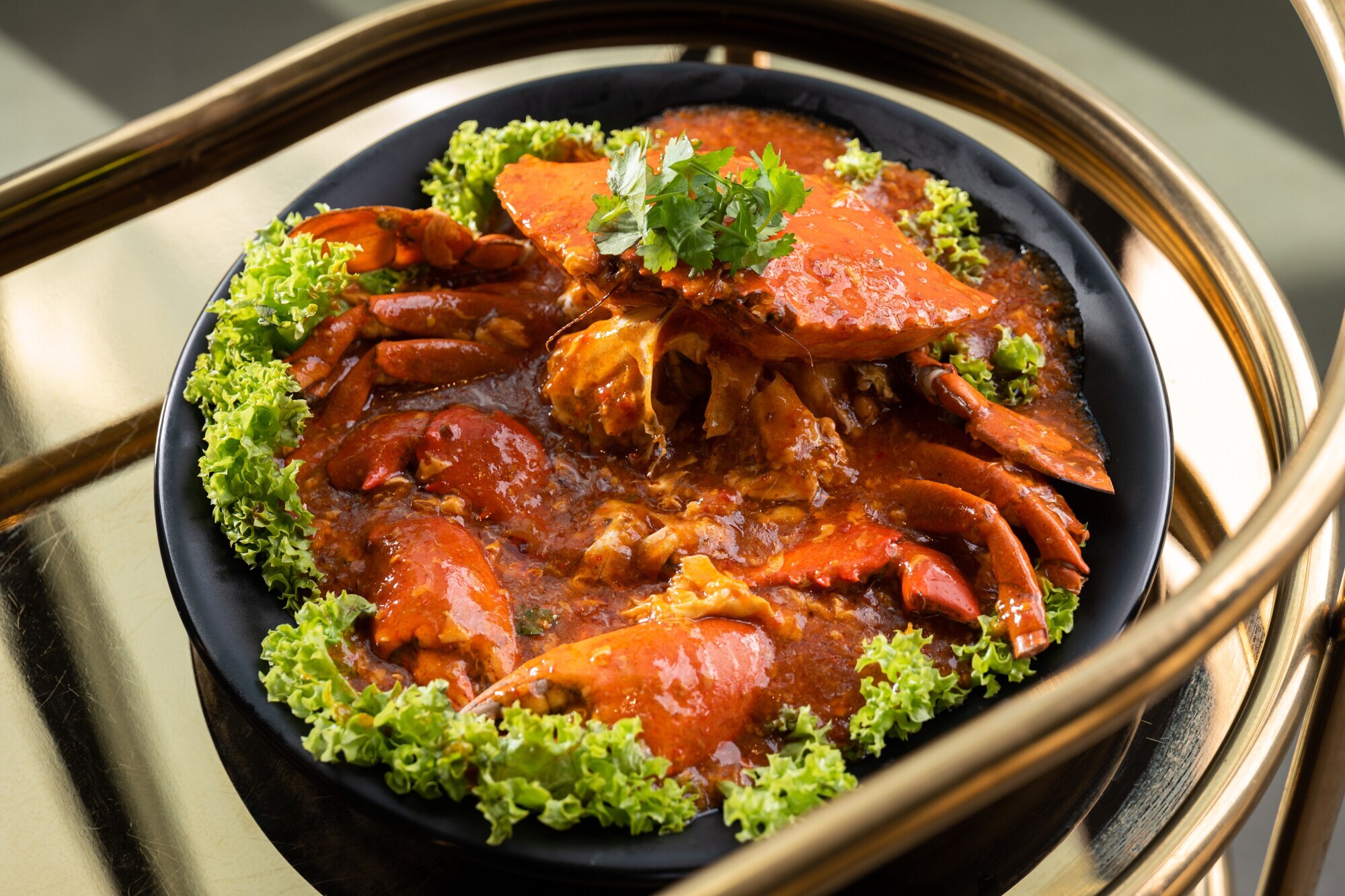 Eine gekochte Krabbe in roter Chilisoße auf einem schwarzen Teller, garniert mit Salatblättern.