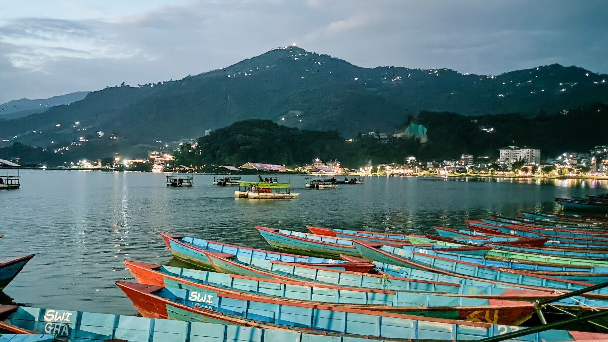 See mit Fischerbooten am Ufer einer Kleinstadt bei Abenddämmerung.