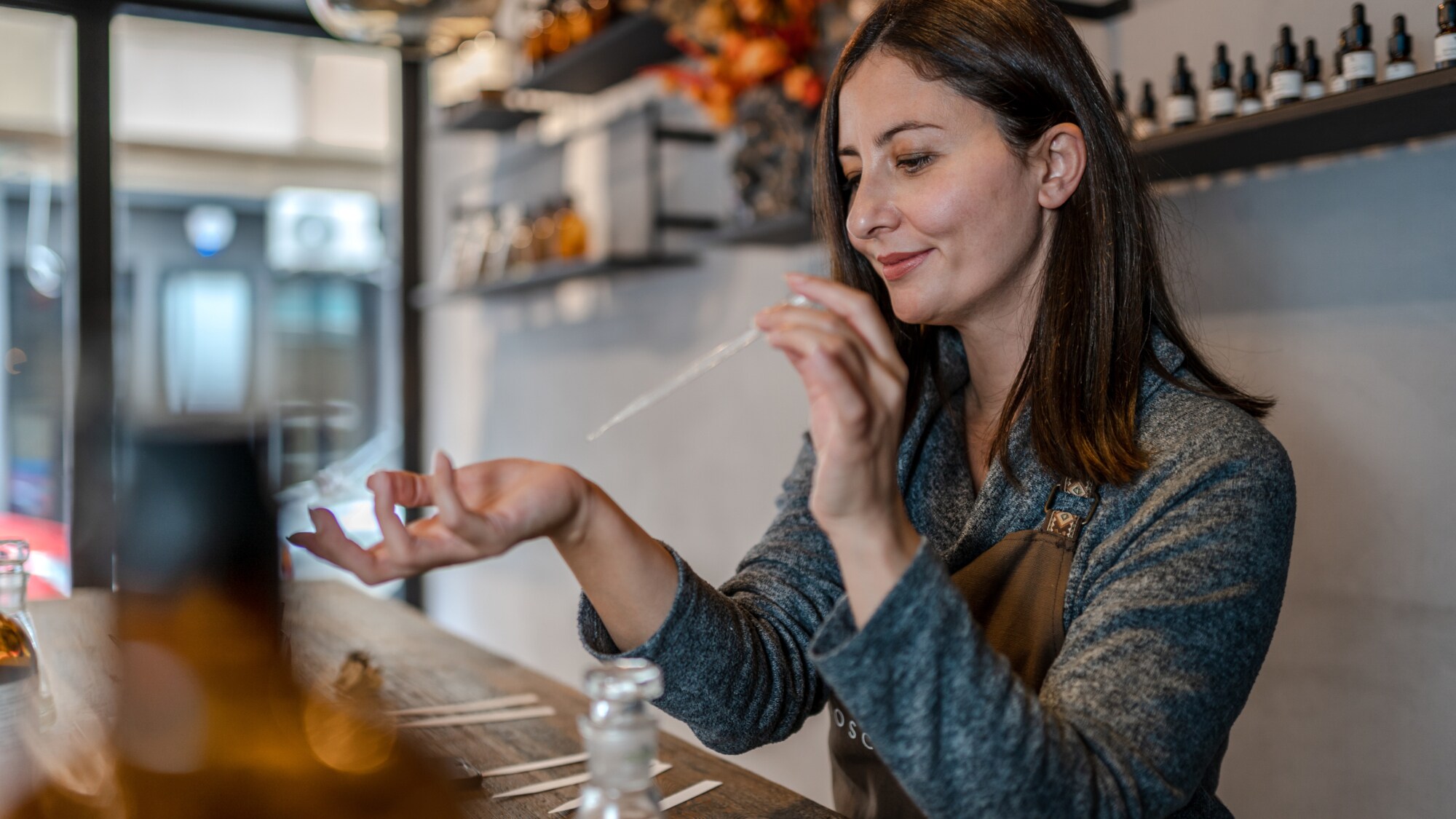 Eine Frau, die an einer Theke steht, auf der mehrere Papierstreifen liegen, träufelt mit einer Pipette etwas auf ihr Handgelenk.