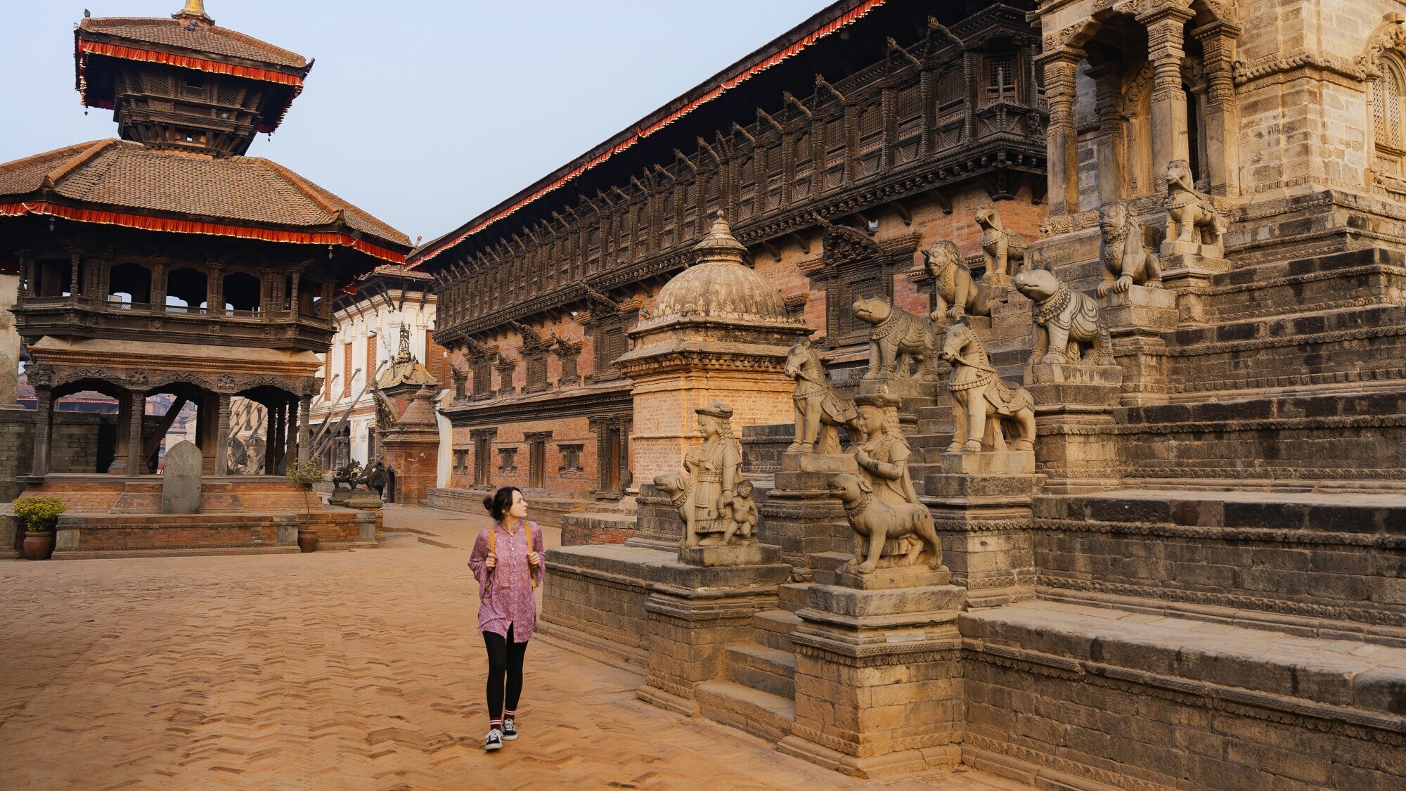 Eine Frau neben Steinskulpturen am Eingang einer Tempelanlage in Bhaktapur.