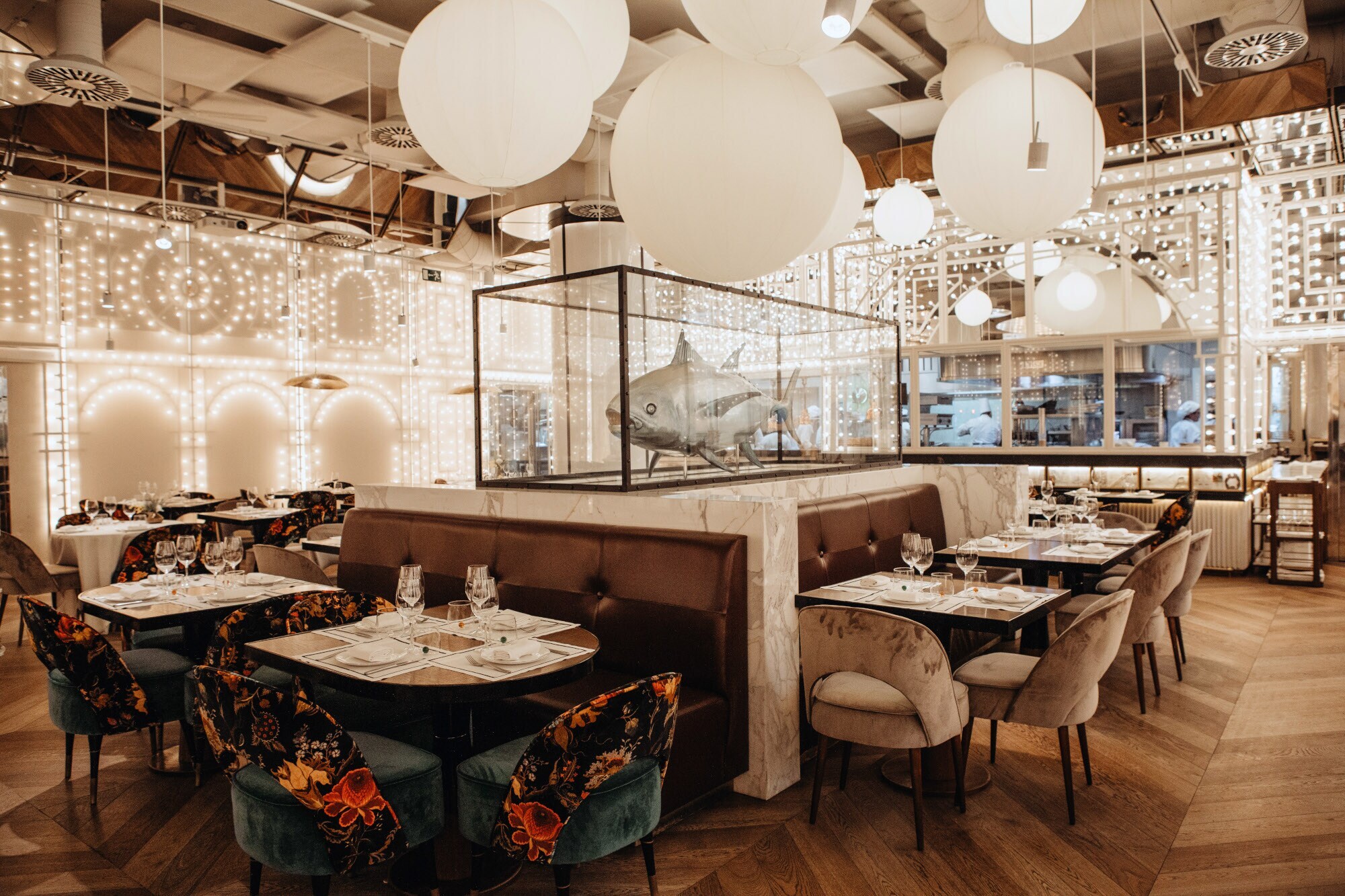 Modernes Restaurant mit zahlreichen Lichtern an Decke und Wänden, im Mittelpunkt eine Haifisch-Skulptur in einem Glaskasten.