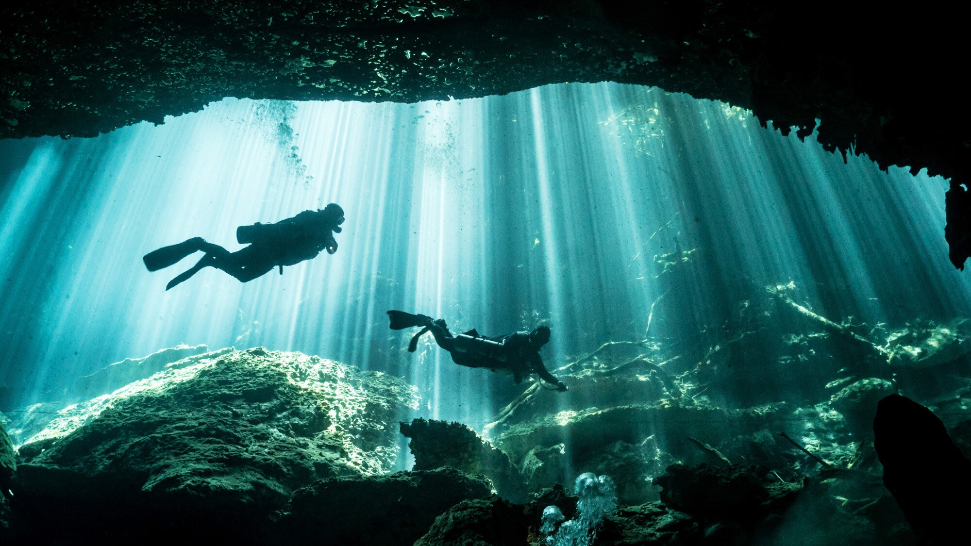 Zwei Taucher schwimmen durch Sonnenstrahlen in einer Unterwasserhöhle. Zwei Taucher schwimmen durch Sonnenstrahlen in einer Unterwasserhöhle.