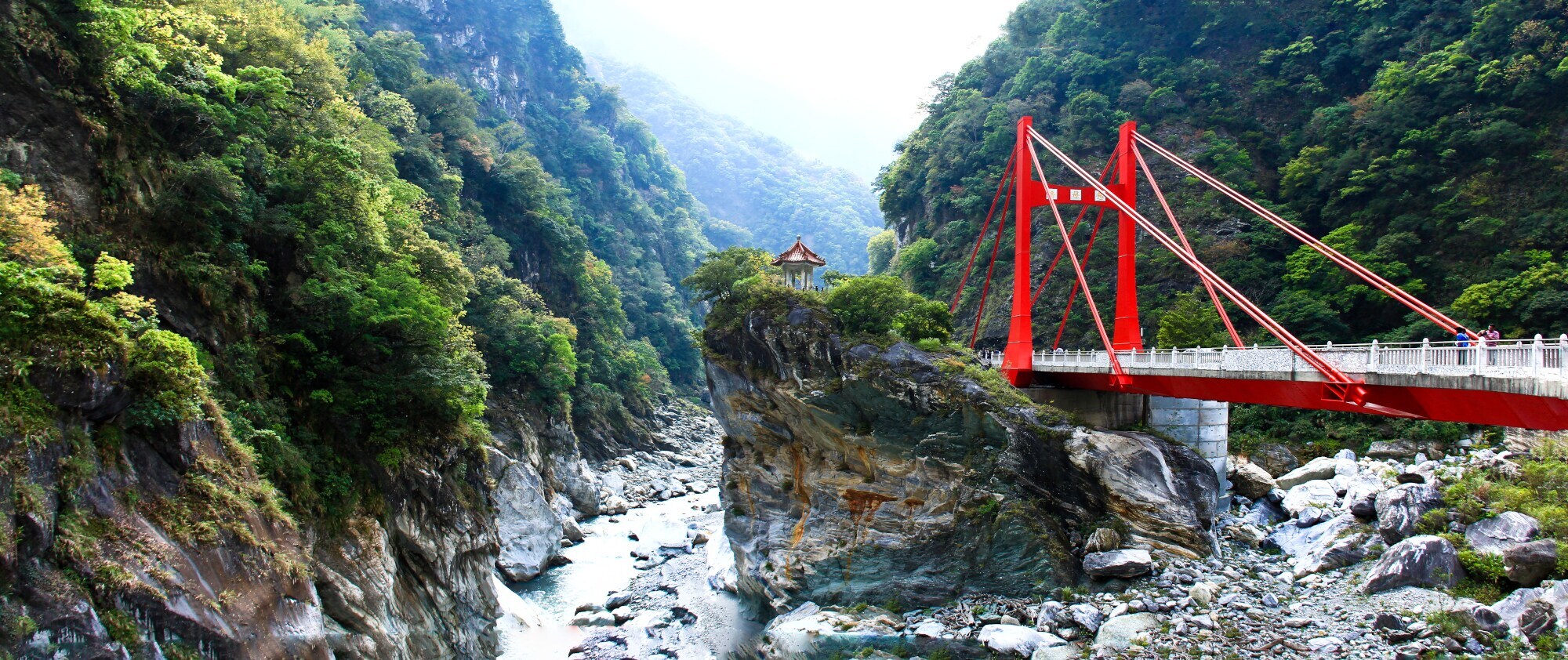 Eine Schlucht an einem Fluss mit roter Hängebrücke.