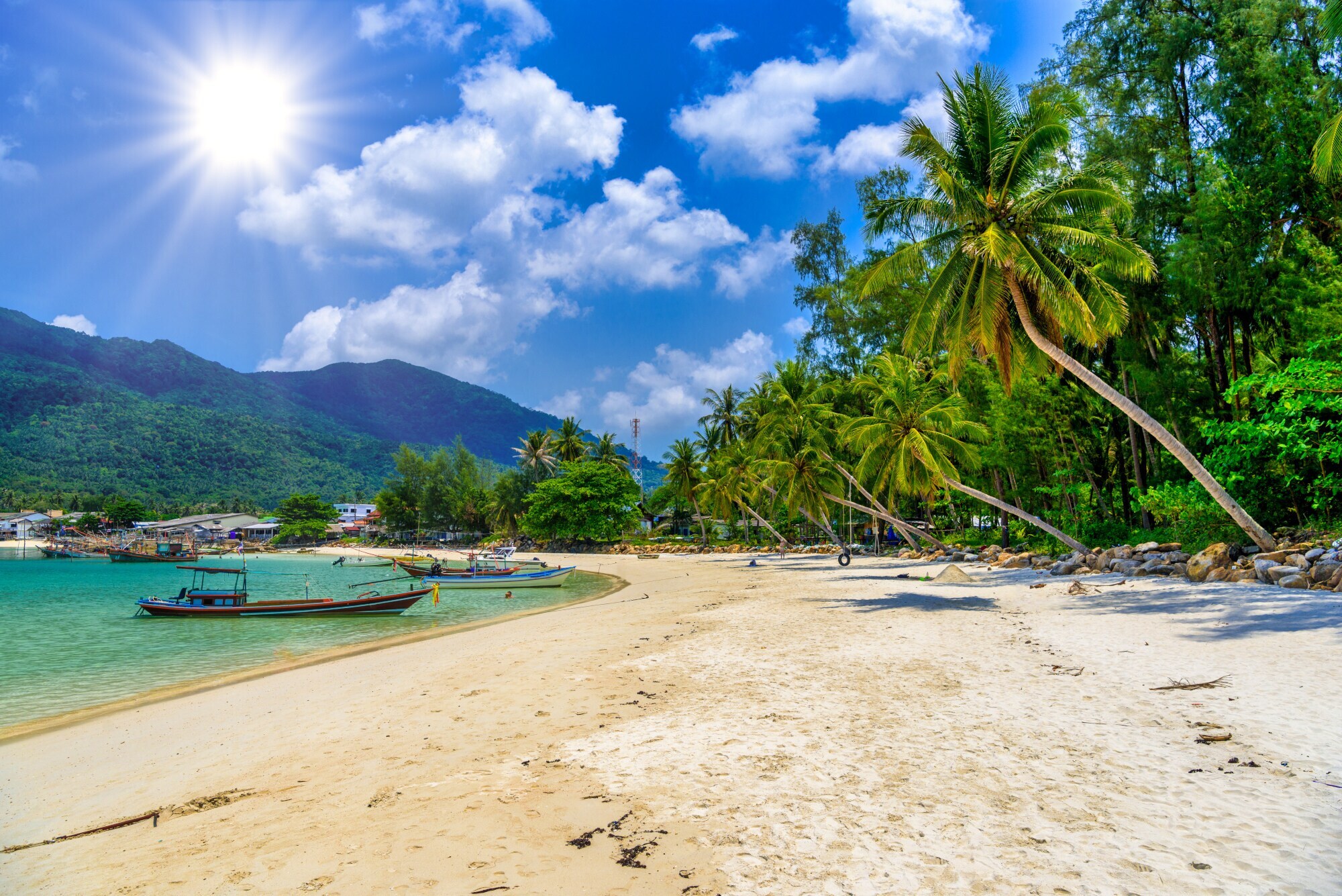 Palmengesäumter Sandstrand an türkisblauem Meer mit Fischerbooten, im Hintergrund eine Hügelkette mit Dschungel. Palmengesäumter Sandstrand an türkisblauem Meer mit Fischerbooten, im Hintergrund eine Hügelkette mit Dschungel.