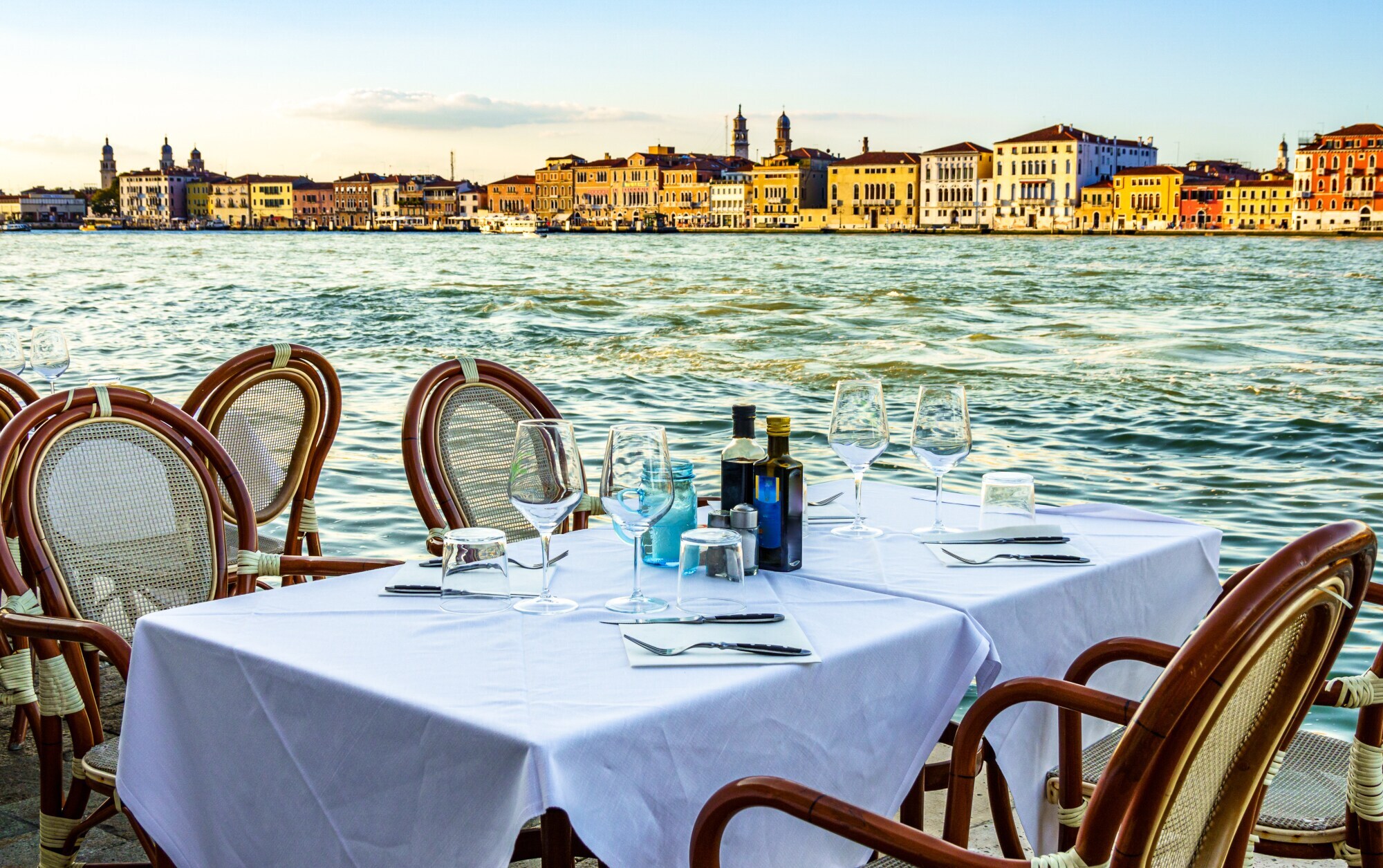Ein gedeckter Tisch im Außenbereich eines Restaurants am Wasser in Venedig.