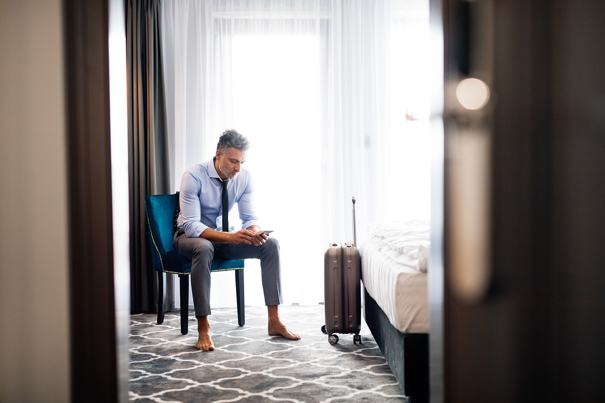 Hotelhacks: Diese 5 Tricks verschaffen dir mehr Komfort Ein Geschäftsmann schaut im Hotelzimmer auf sein Smartphone.
