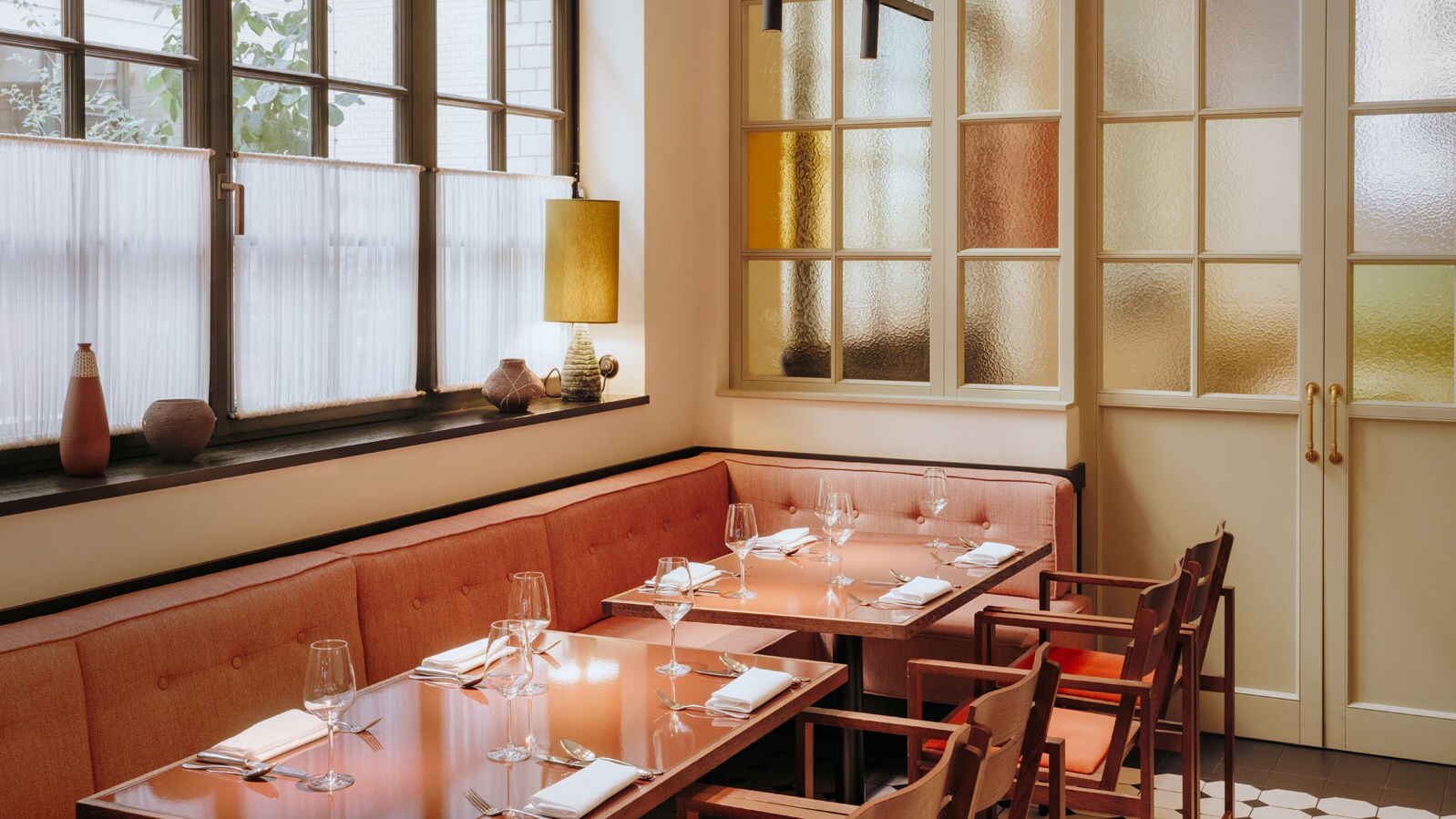 Interieur mit gedeckten Tischen und korallfarbenen Sitzmöbeln am Fenster.