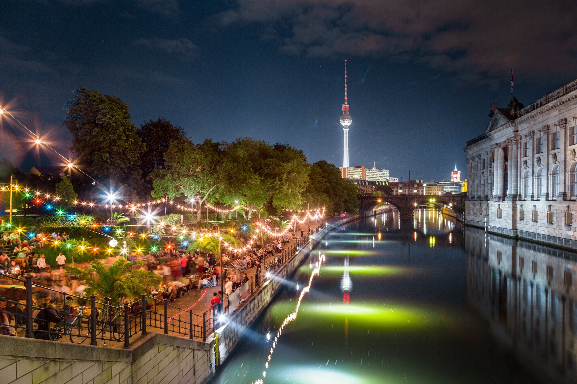 Personen in einer Strandbar am Spreeufer an der Berliner Museumsinsel bei Nacht, im Hintergrund ein beleuchteter Fernsehturm. Personen in einer Strandbar am Spreeufer an der Berliner Museumsinsel bei Nacht, im Hintergrund ein beleuchteter Fernsehturm.