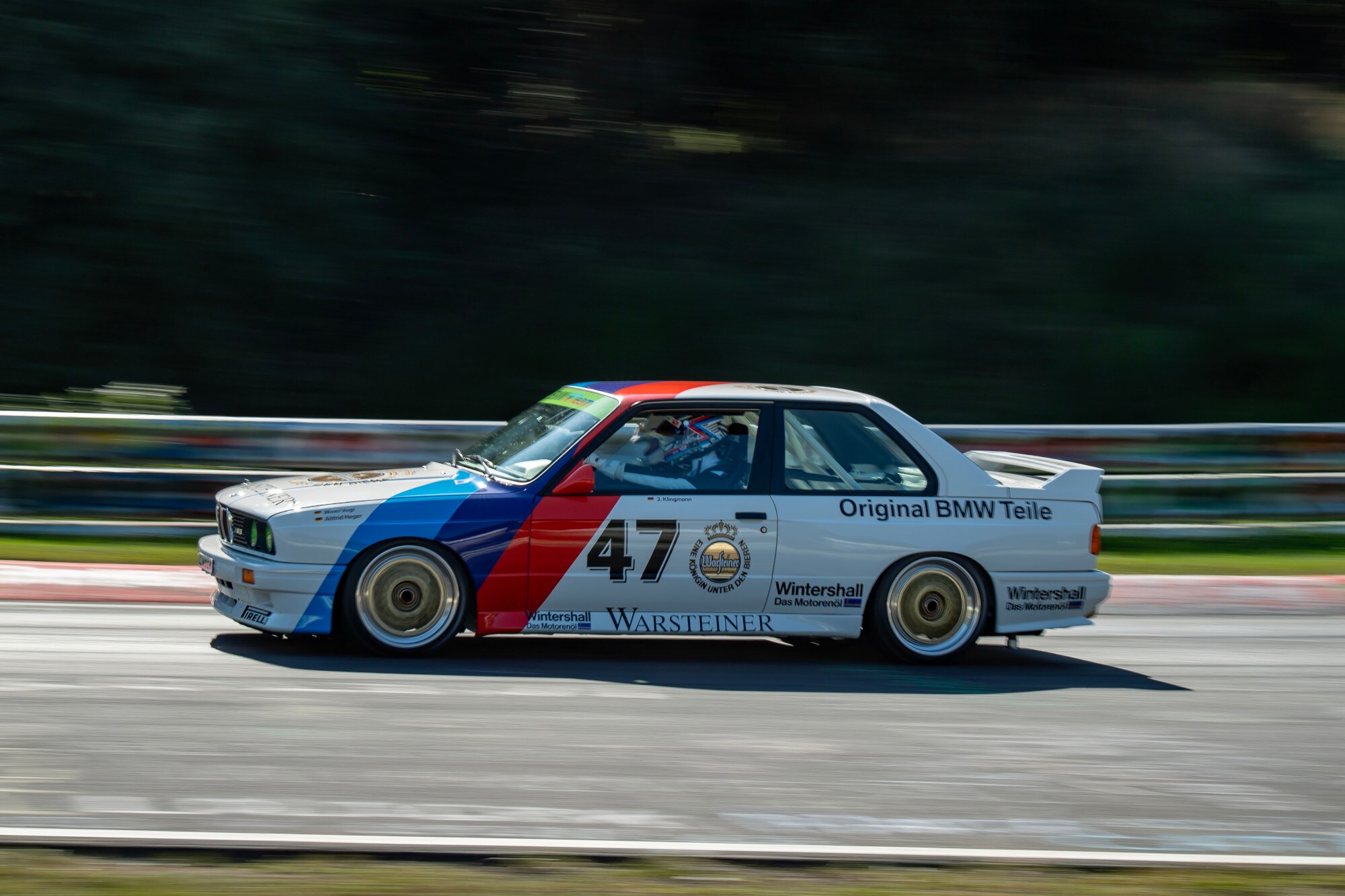 Ein fahrender BMW M3 E30 Rennwagen auf einer Straße.