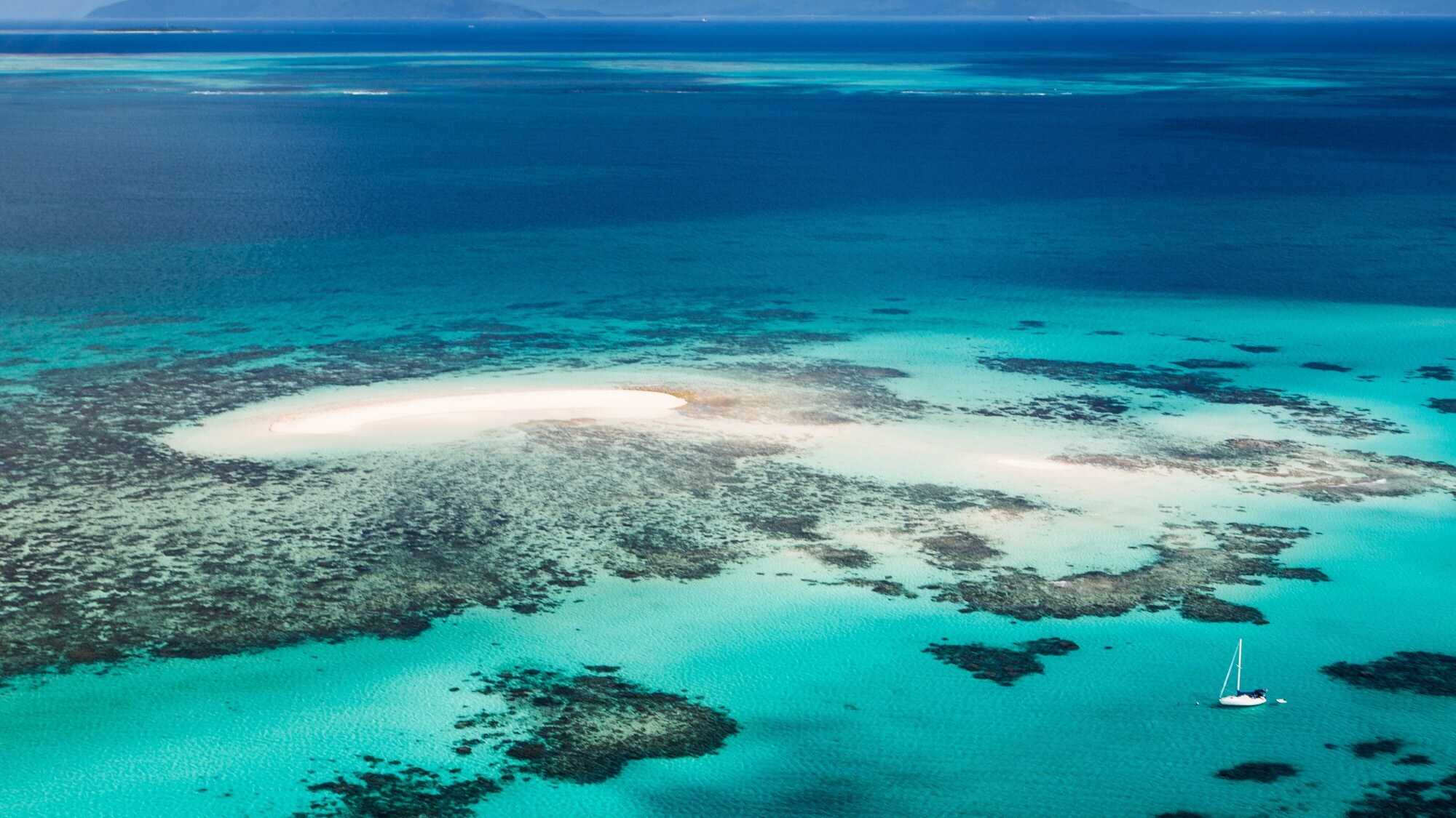 Luftaufnahme des Great Barrier Reefs mit Segelboot im türkisblauen Wasser. Luftaufnahme des Great Barrier Reefs mit Segelboot im türkisblauen Wasser.