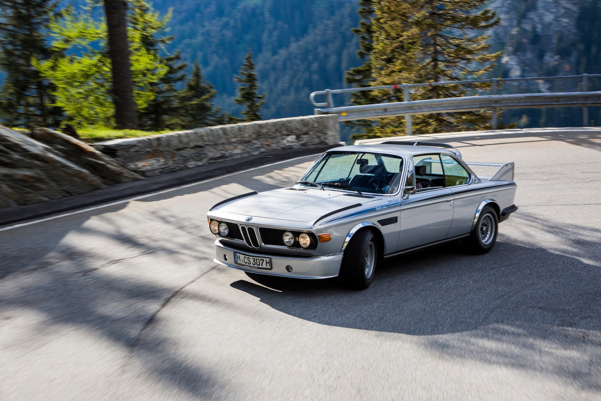 Ein fahrender silberner BMW 3.0 CSL in einer Kurve auf einer Straße in den Bergen. Ein fahrender silberner BMW 3.0 CSL in einer Kurve auf einer Straße in den Bergen.