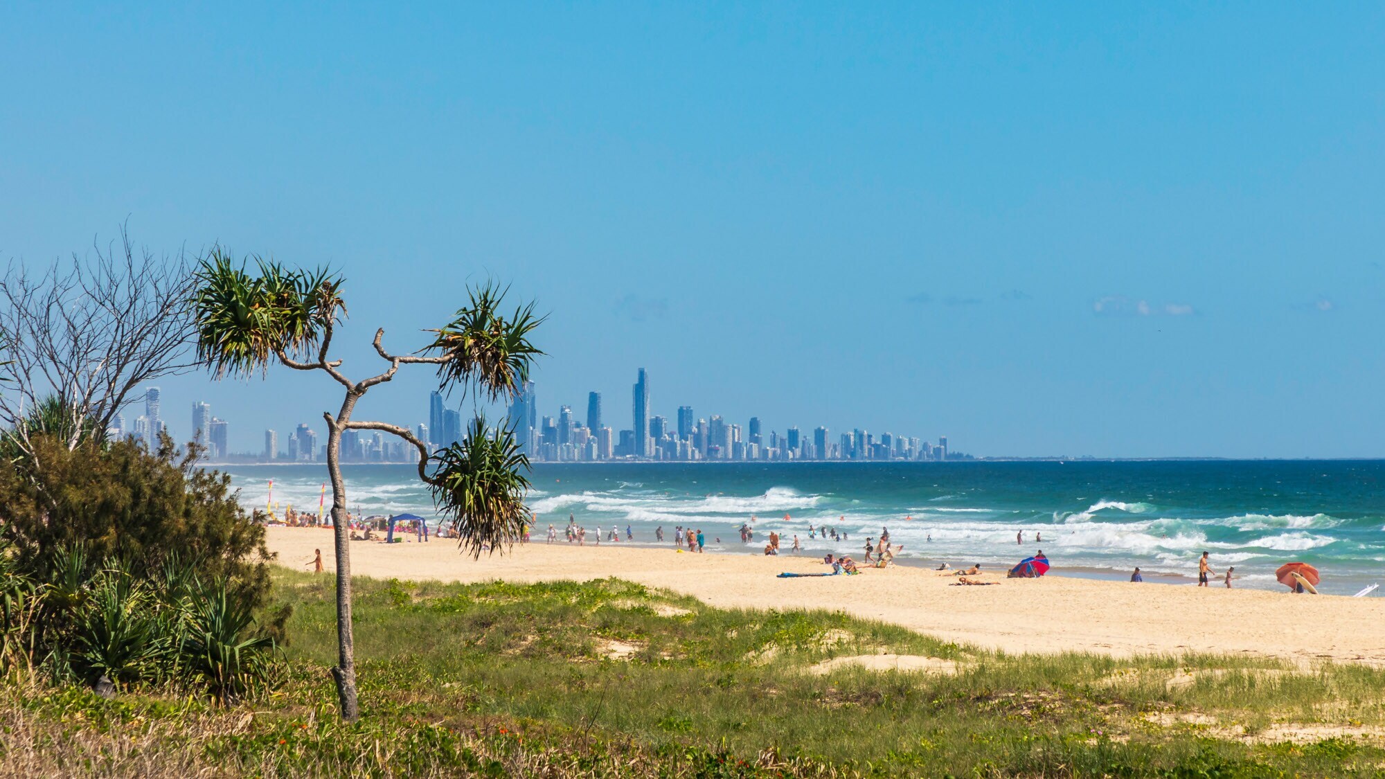 Belebter, weitläufiger Sandstrand am welligen Meer, im Hintergrund eine Skyline. Belebter, weitläufiger Sandstrand am welligen Meer, im Hintergrund eine Skyline.