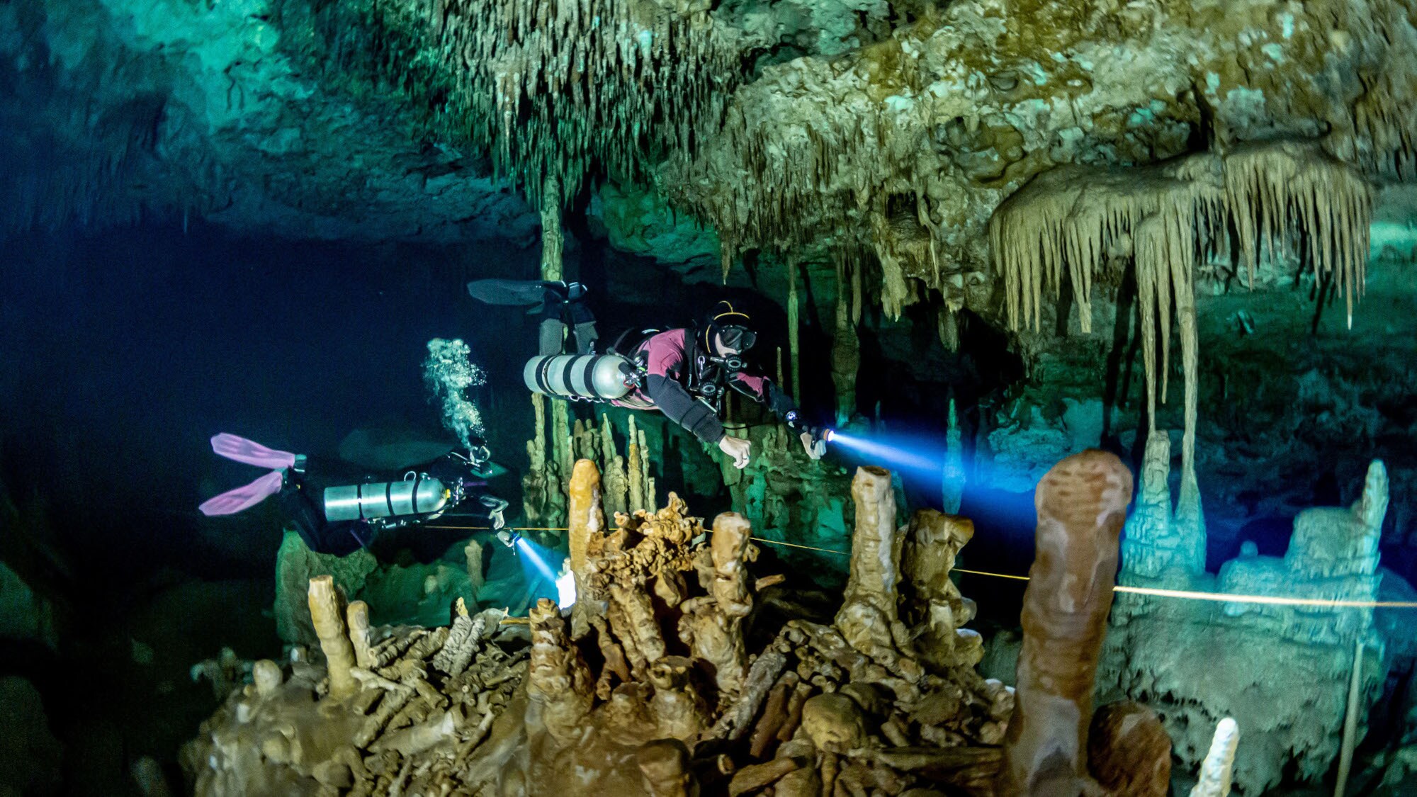 Zwei Personen in Tauchausrüstung, die durch eine Unterwasser-Tropfsteinhöhle mit Lampen schwimmen. Zwei Personen in Tauchausrüstung, die durch eine Unterwasser-Tropfsteinhöhle mit Lampen schwimmen.