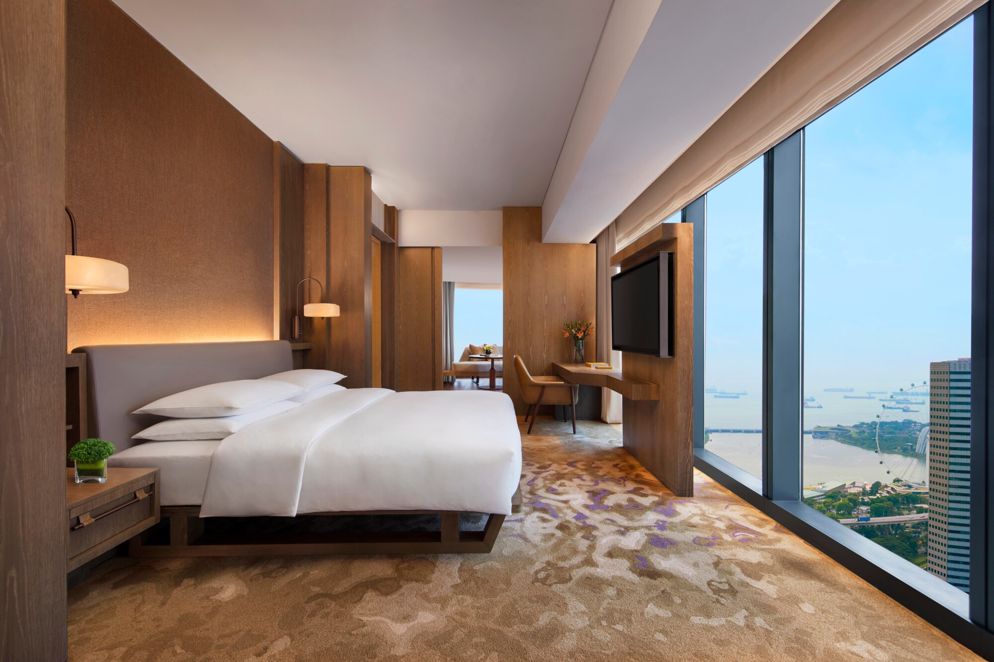 Moderne Hotelsuite mit Holzelementen und Aussicht auf das Hafengebiet von Singapur durch raumhohe Panoramafenster. Moderne Hotelsuite mit Holzelementen und Aussicht auf das Hafengebiet von Singapur durch raumhohe Panoramafenster.