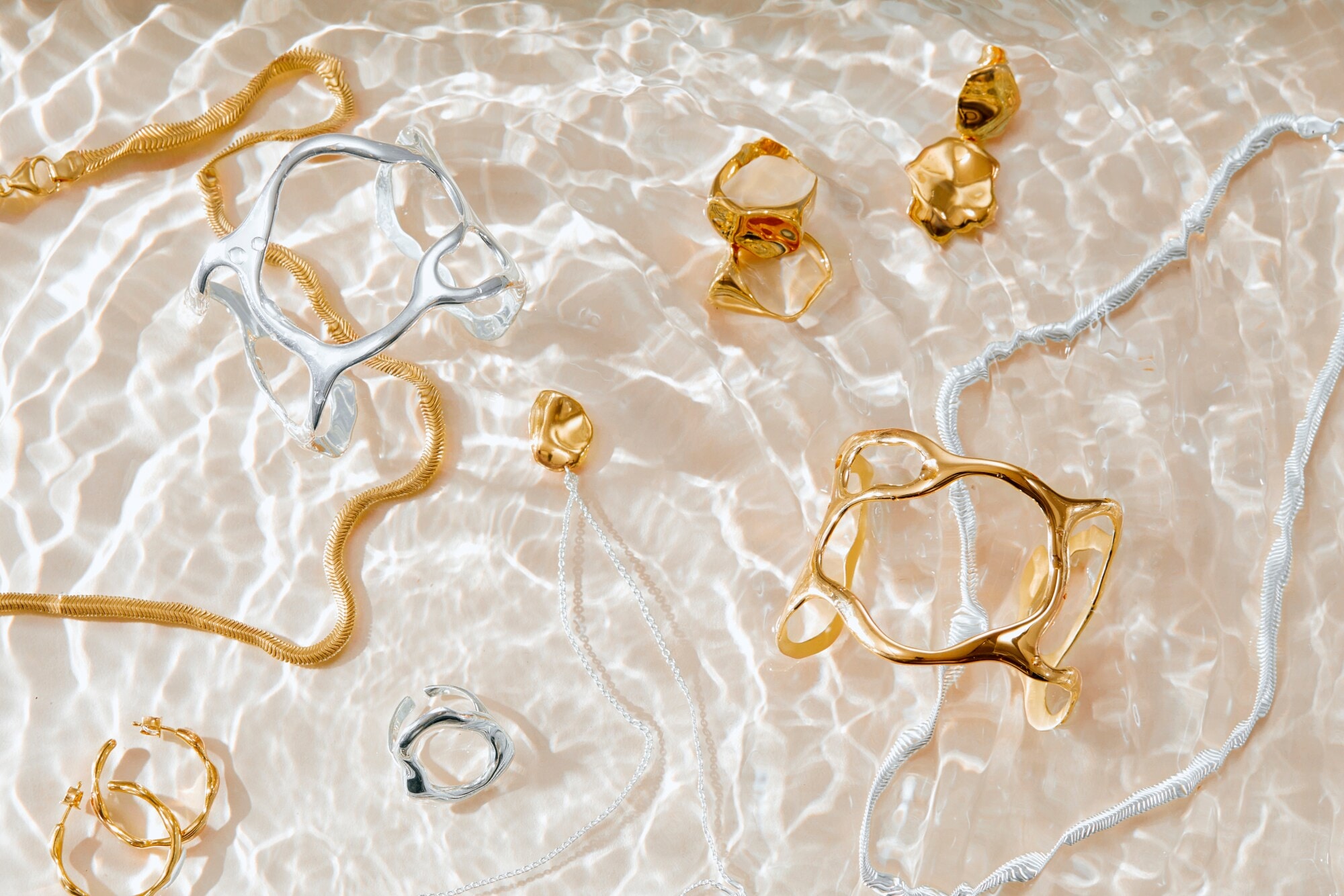 Unterschiedliche Schmuckstücke in Gold und Silber liegen auf Wasser mit Lichtspiel Unterschiedliche Schmuckstücke in Gold und Silber liegen auf Wasser mit Lichtspiel