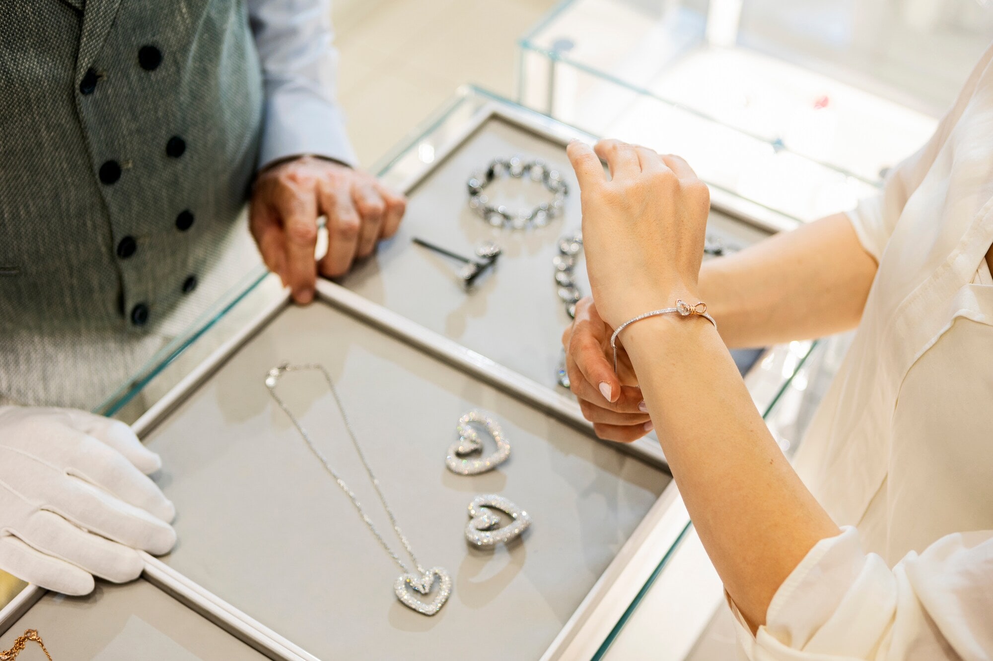Der Arm einer Frau, die gerade ein Diamantarmband anzieht, da drunter ein Tisch mit mehreren Schmuckstücken. Der Arm einer Frau, die gerade ein Diamantarmband anzieht, da drunter ein Tisch mit mehreren Schmuckstücken.