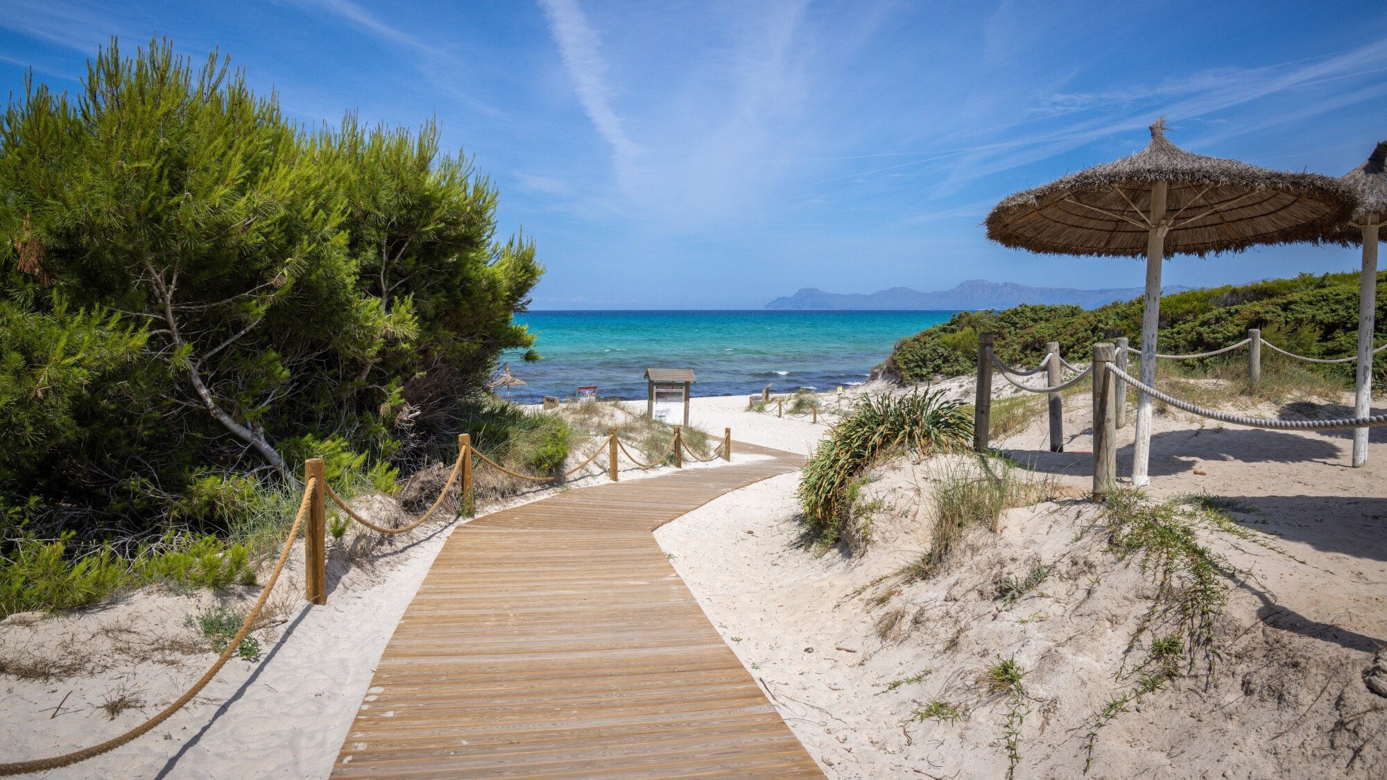 Ein Holzsteg führt durch Dünen zu einem Sandstrand am türkisblauen Meer. Ein Holzsteg führt durch Dünen zu einem Sandstrand am türkisblauen Meer.
