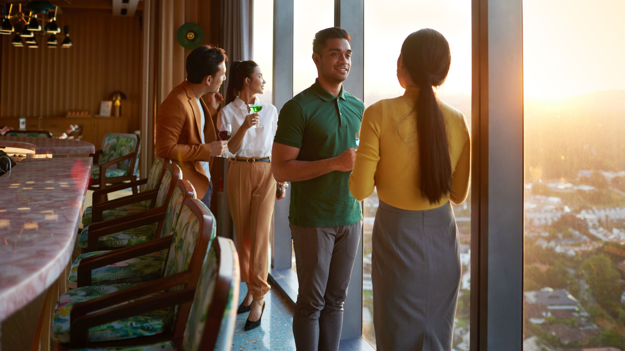 Vier elegant-lässig gekleidet Personen stehen mit Getränken an einem Fenster in einer Bar mit Panoramablick. Vier elegant-lässig gekleidet Personen stehen mit Getränken an einem Fenster in einer Bar mit Panoramablick.
