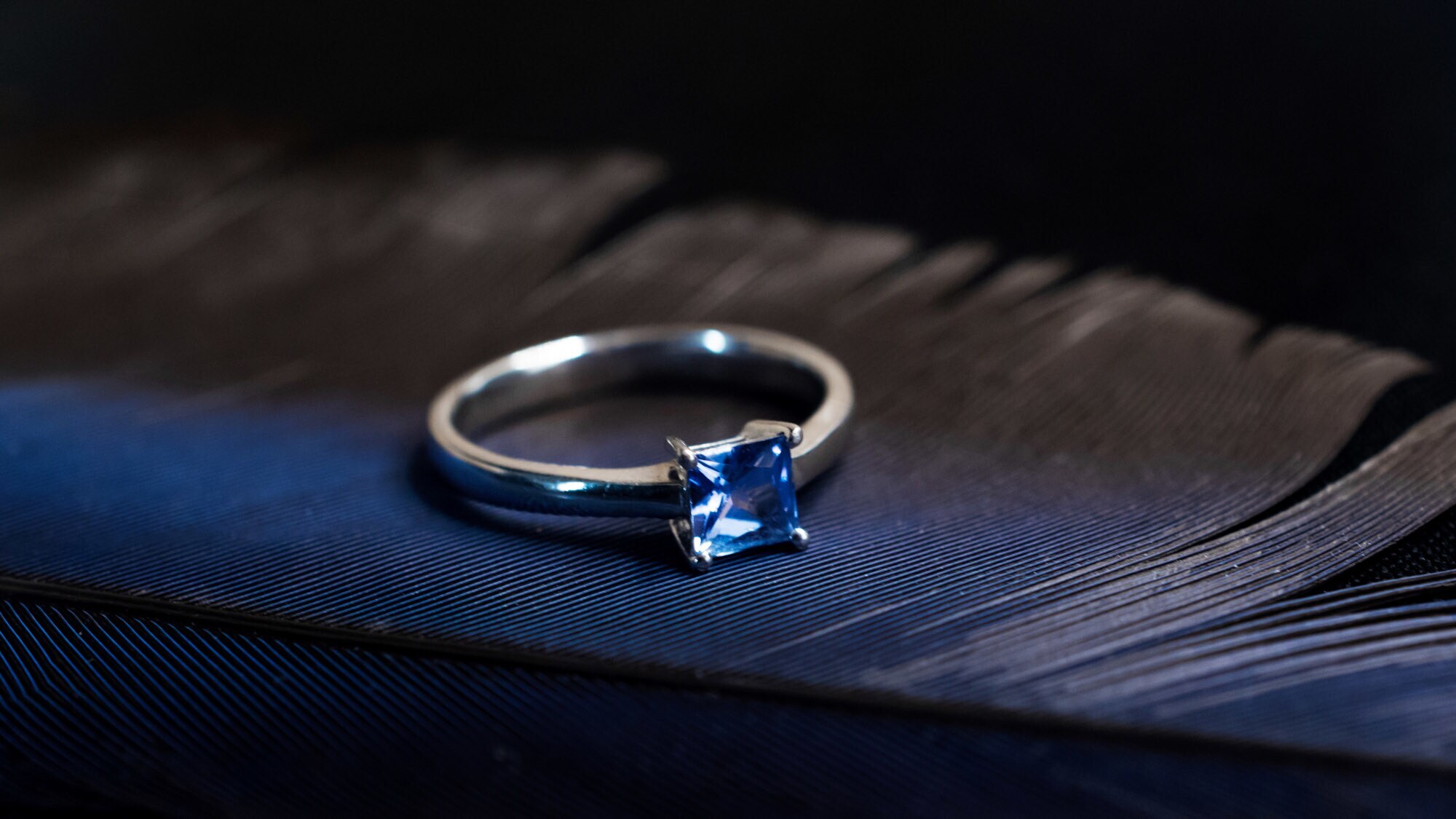 Ein Silberring mit blauem Edelstein auf einer schwarzen Feder.