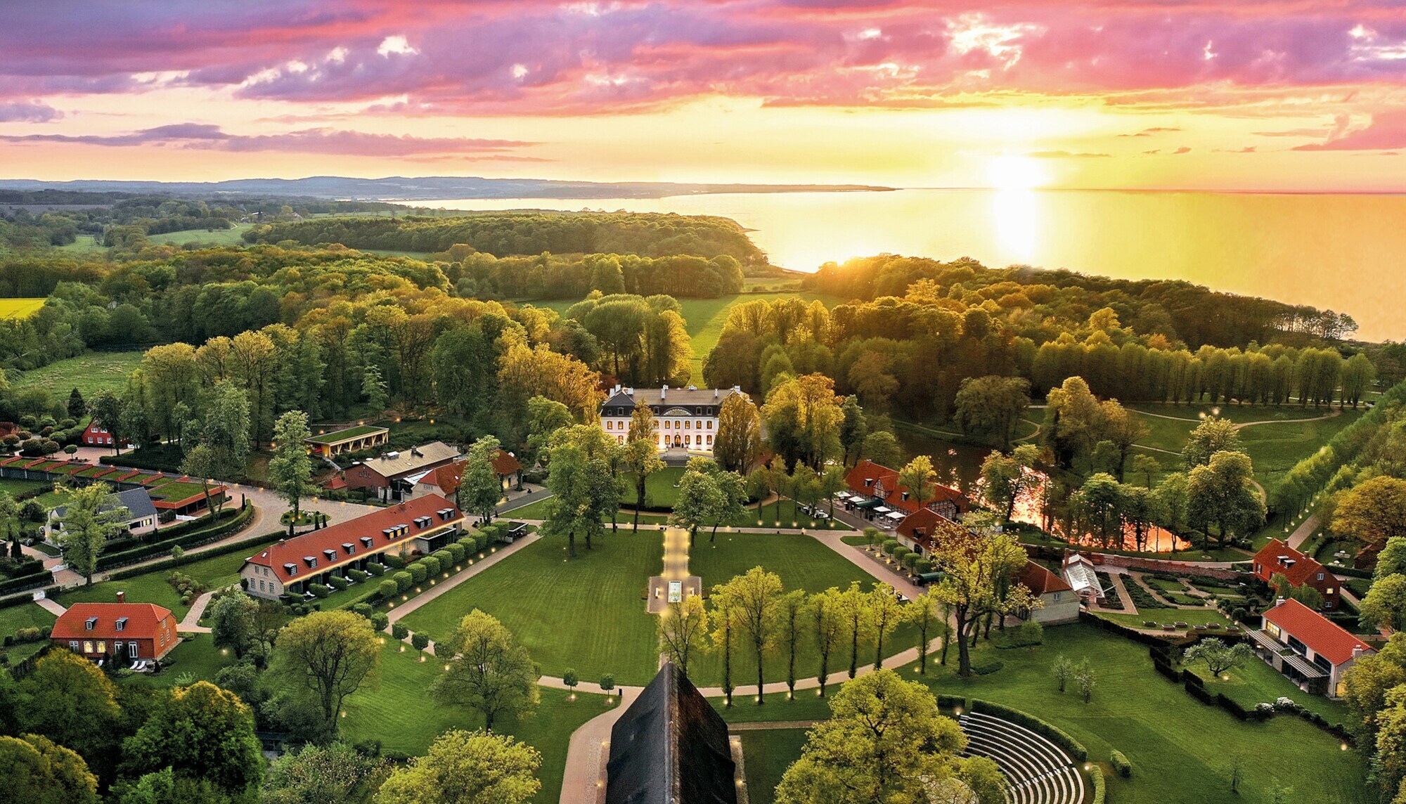 Luxuriöses Hotelresort mit Park- und Waldlandschaft an Meeresküste bei Sonnenuntergang.