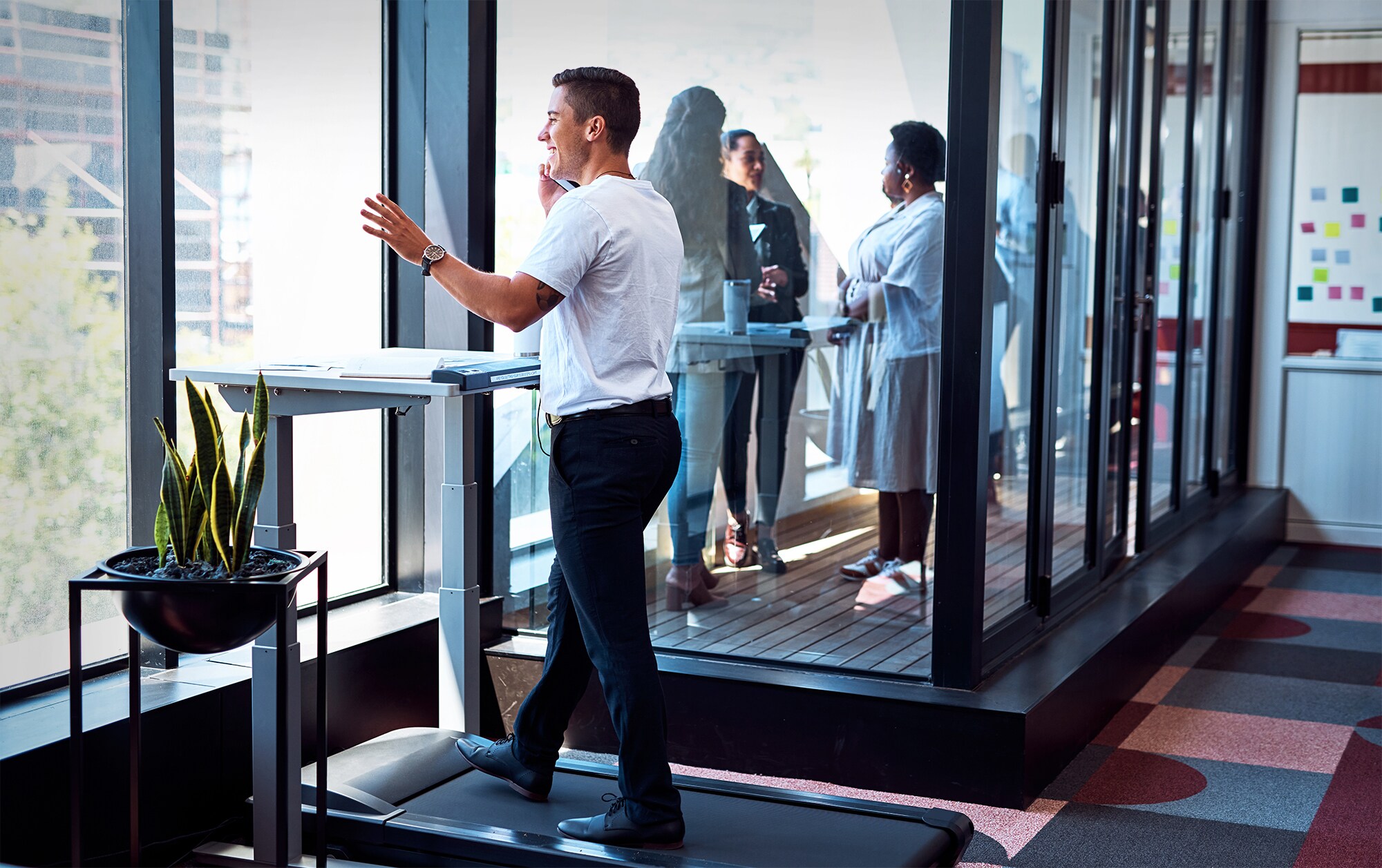 Biohacking im Büro: Gesundheitsgadgets fürs Business Ein Geschäftsmann trainiert im Büro auf einem Laufband und telefoniert dabei.