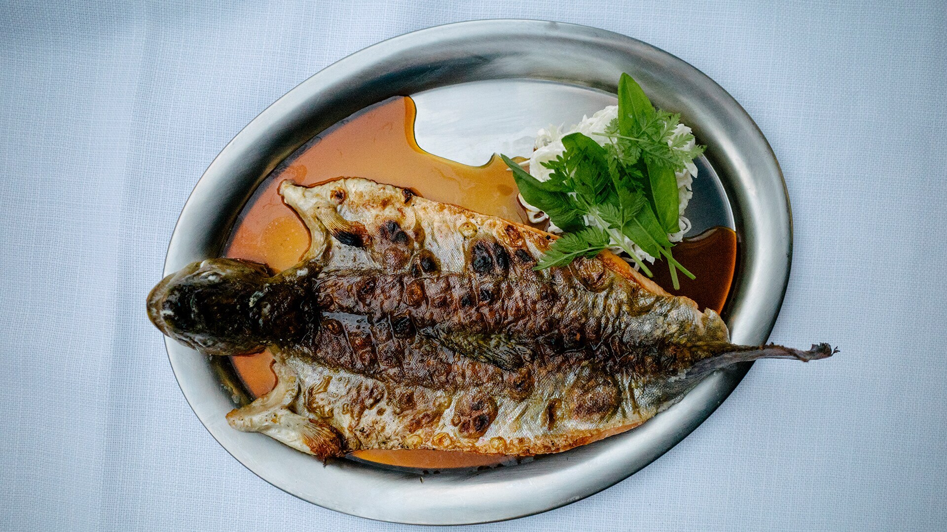 Aufsicht eines gebratenen Bachsaiblings mit Garum auf einem silbernen Teller.