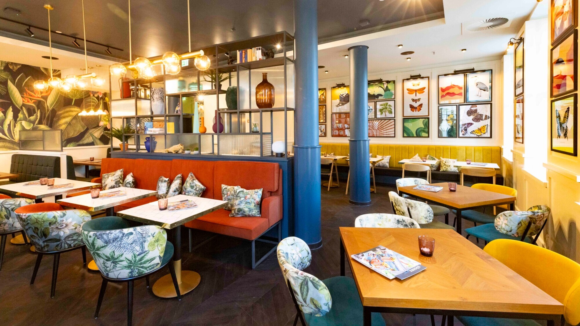 Innenraum des modern eingerichteten ALEX Restaurants an der Frauenkirche in Dresden, das mit großen Leuchten und einer Wandtapete mit Pflanzenmuster dekoriert ist.