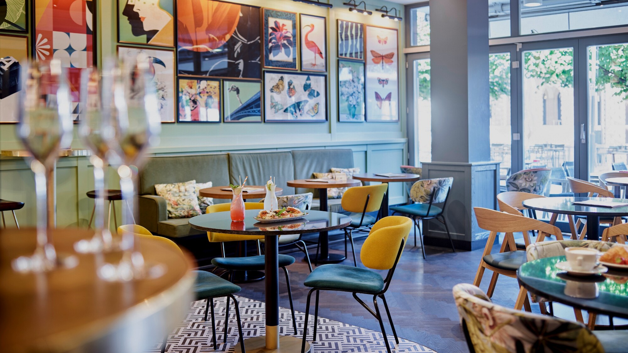 Innenraum des Restaurants ALEX in Mainz mit verschiedenen Stühlen, dunklen Metalltischen, dunklem Holzboden und einer Galleriewand.