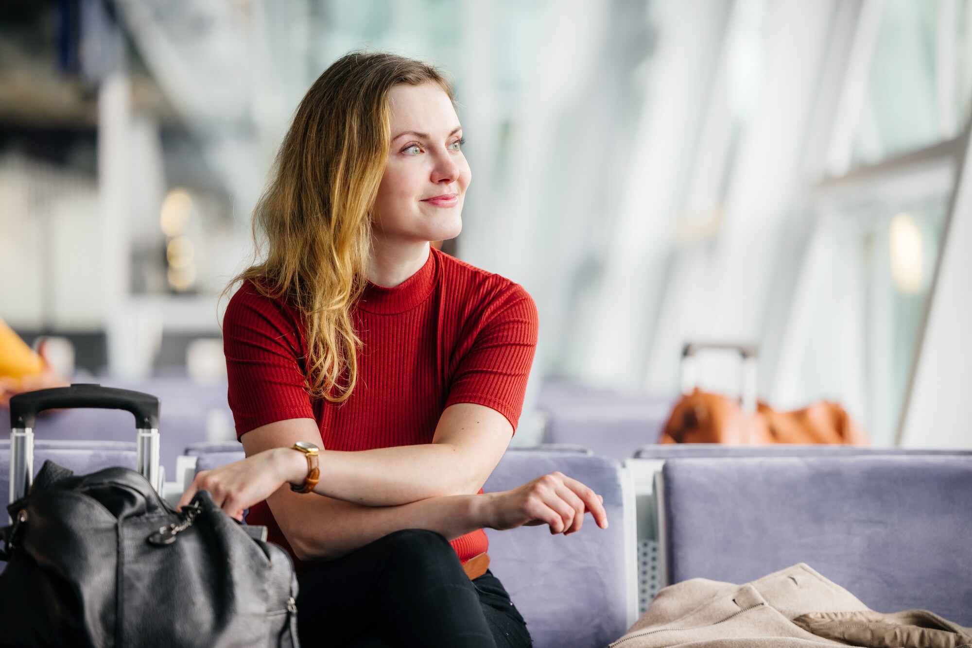 Eine Frau sitzt lächelnd im Wartebereich in einem Flughafenterminal.